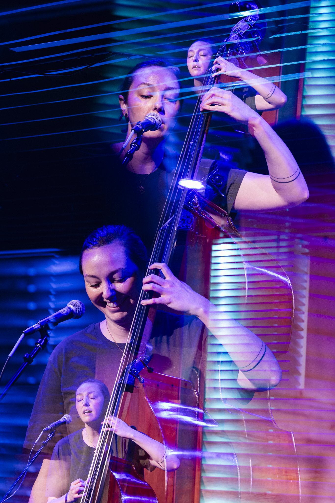 Multiple layered images of a woman playing a double bass and singing into a microphone, with colorful stage lighting, creating a motion effect.