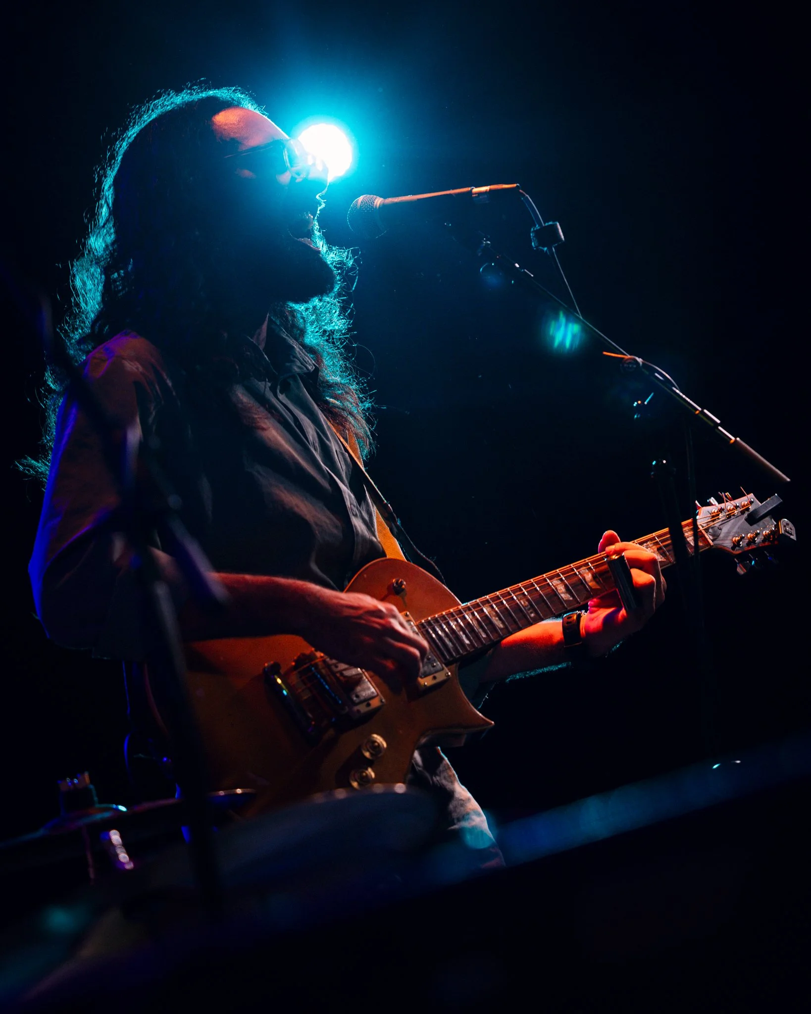 A silhouette of a musician playing an electric guitar and singing into a microphone on stage with blue lighting.