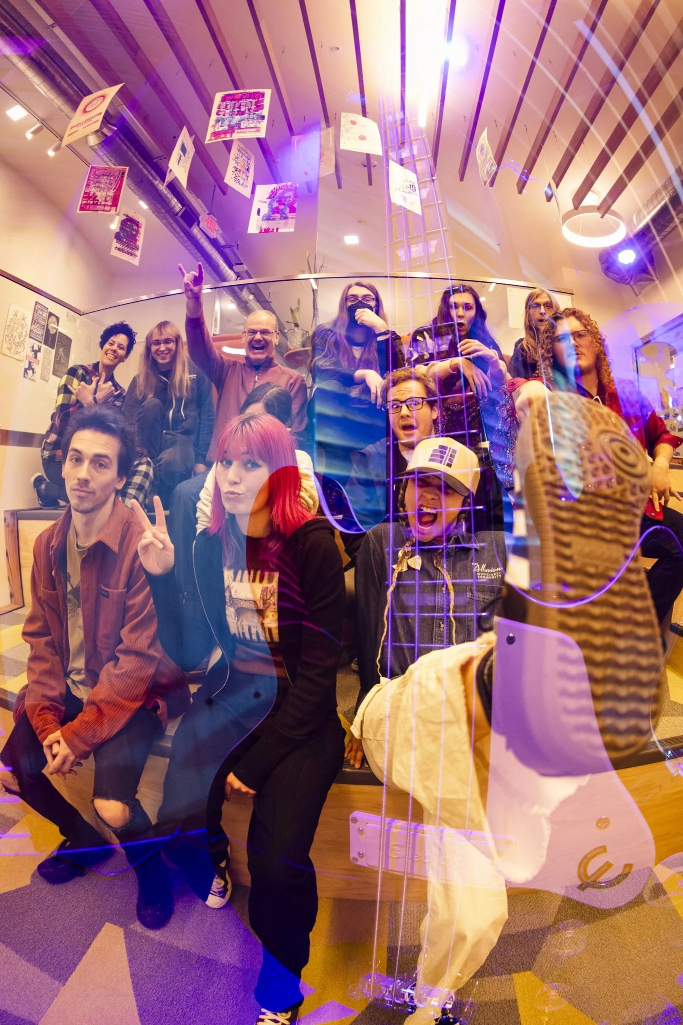 A group of people inside a glass room with colorful lighting, taking a group photo. The photo is taken through the glass, creating reflections and a layered effect.