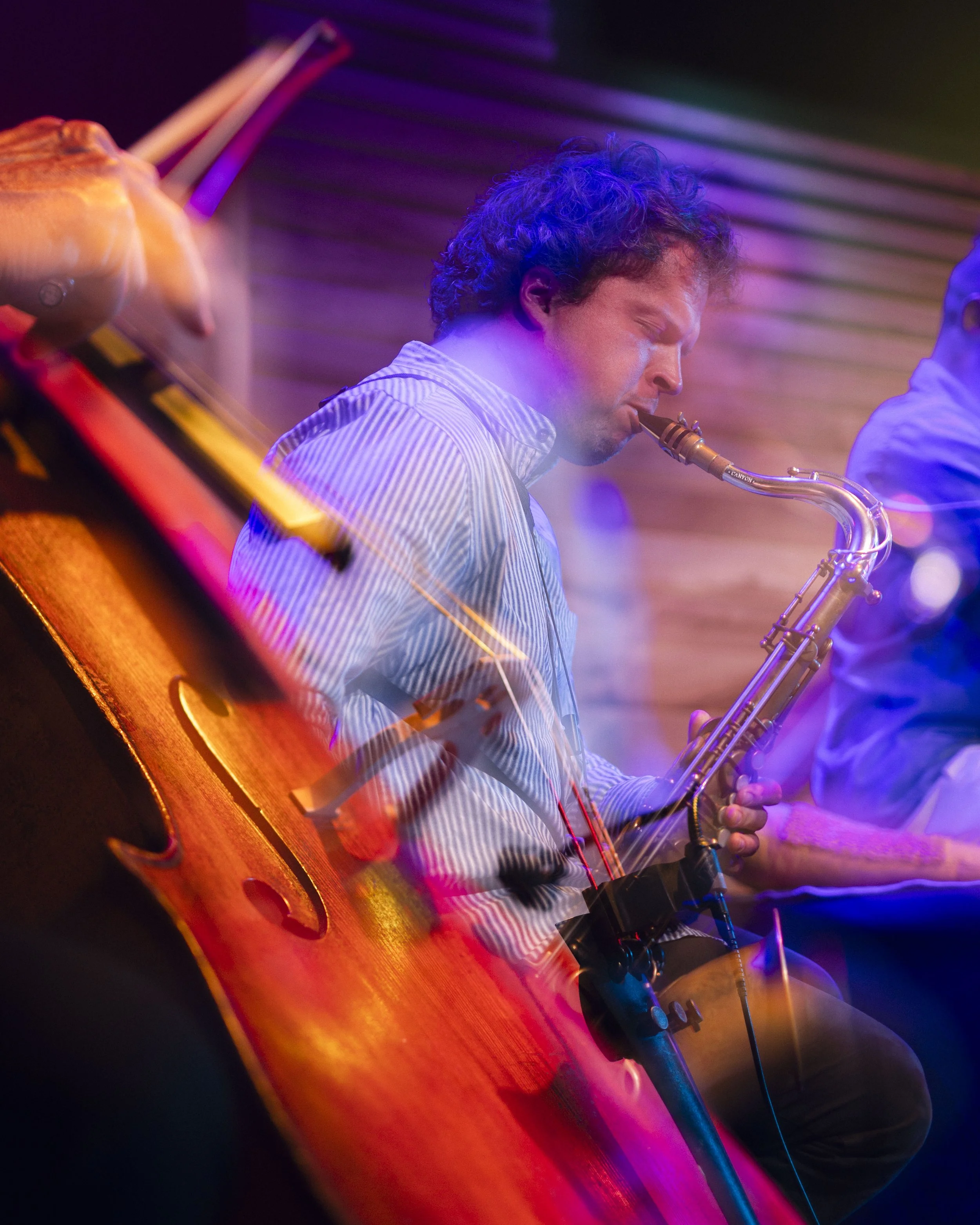 A musician playing a saxophone and a guitar, immersed in colorful stage lighting.