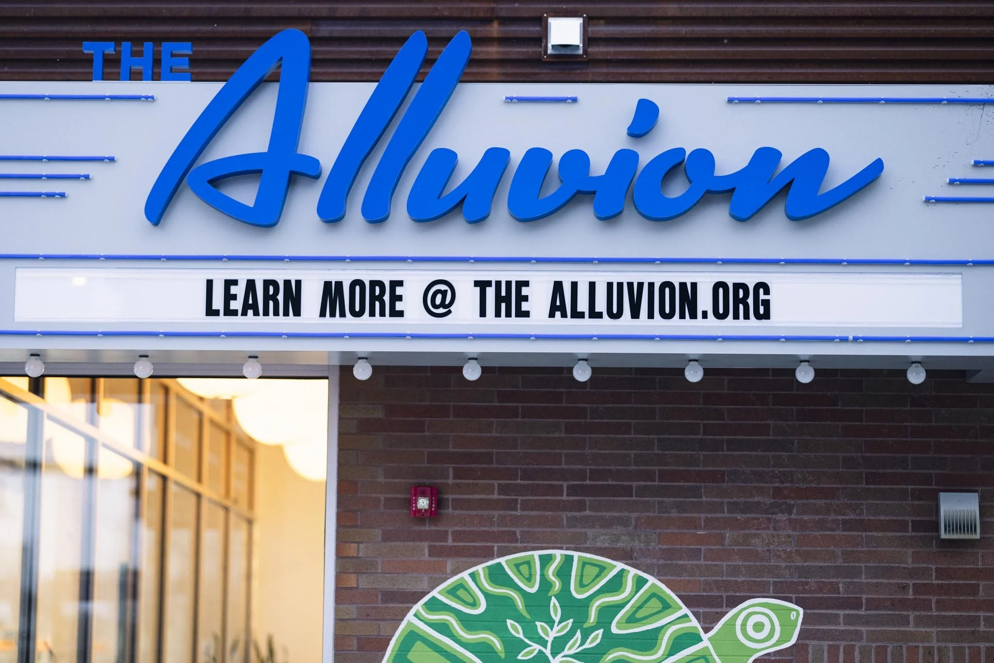 Sign for The Alluvion with a message to learn more at thealluvion.org and a green turtle illustration below.