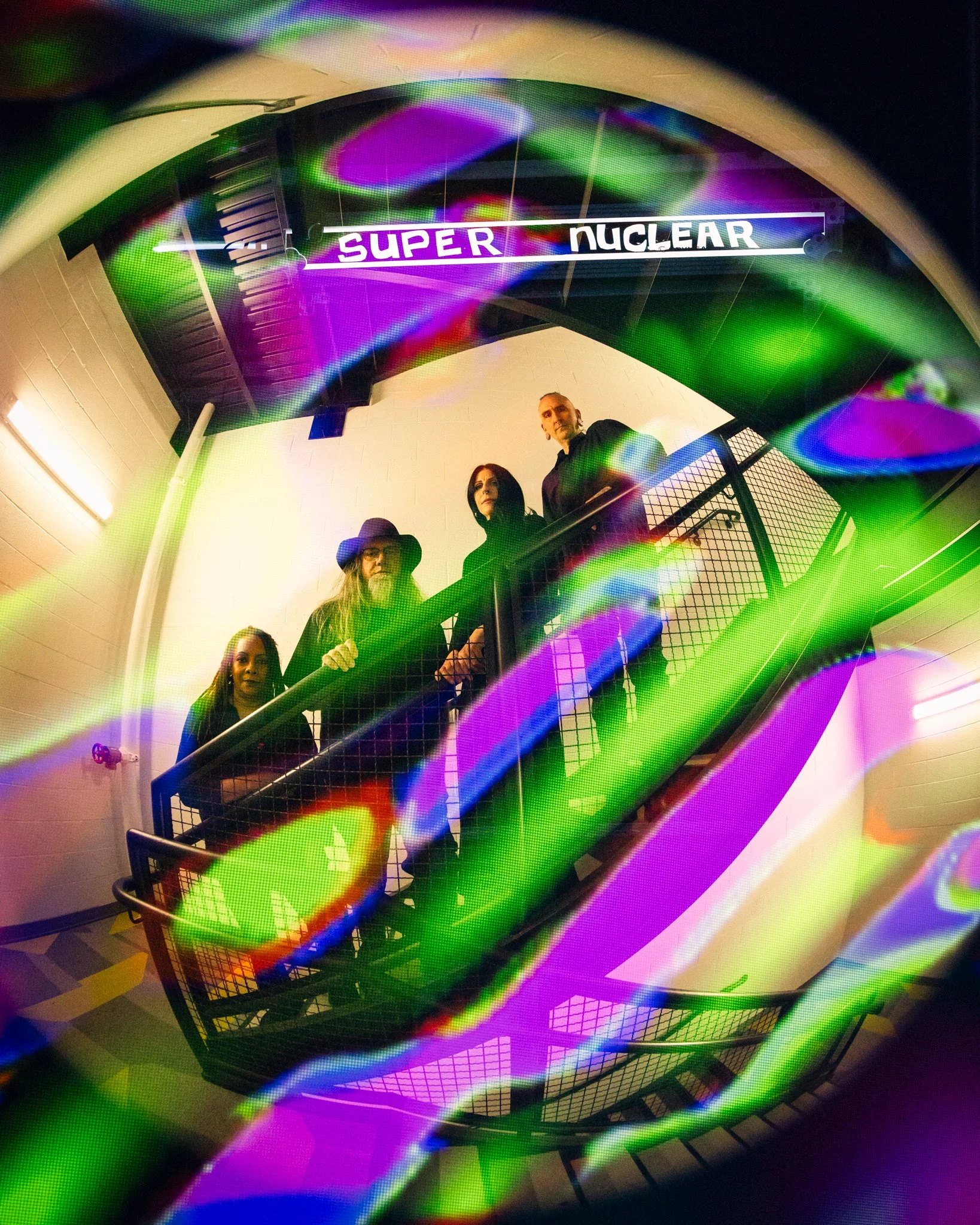 Four people standing on a staircase with a colorful, abstract overlay and a sign reading 'SUPER NUCLEAR' in the background.
