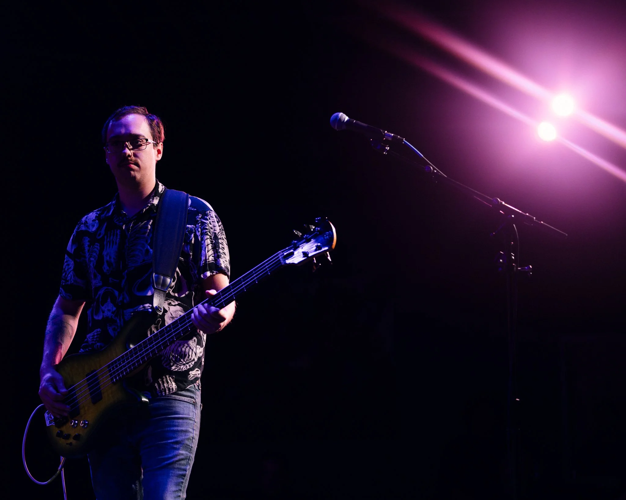A man playing a guitar on stage with purple and pink stage lights shining in the background.