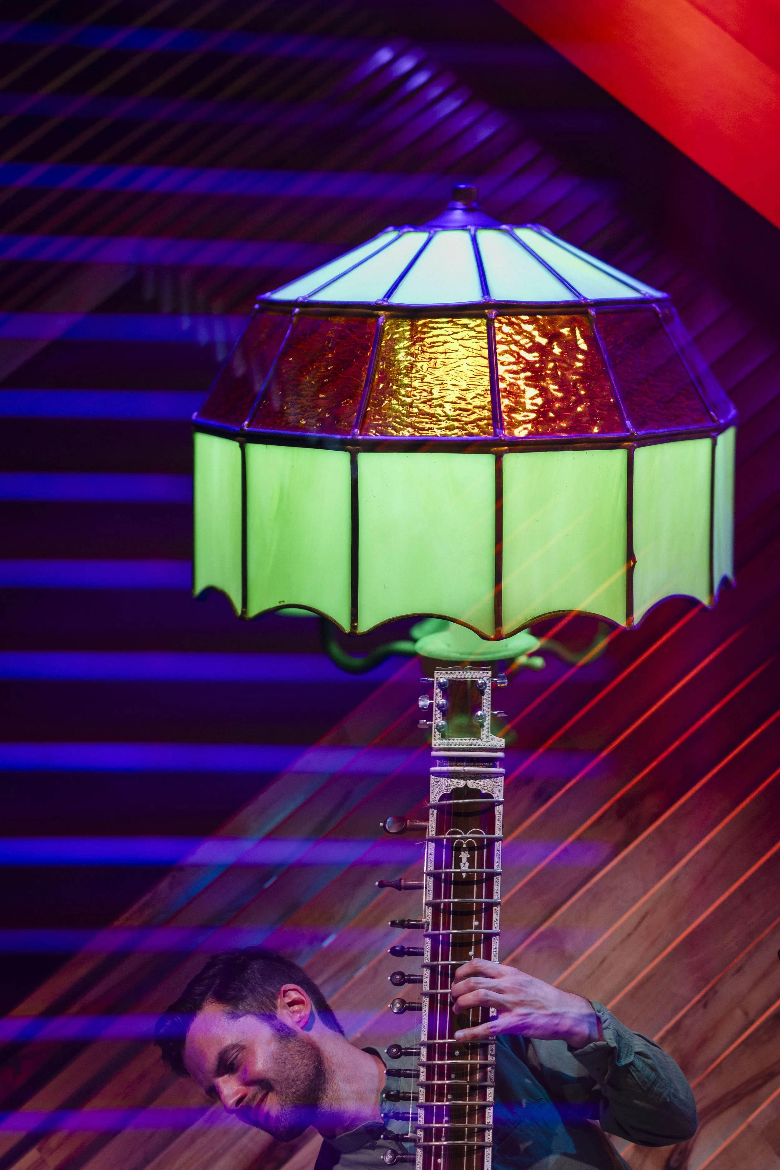 A person is holding a tall, colorful lamp that combines a guitar and a stained glass lampshade.