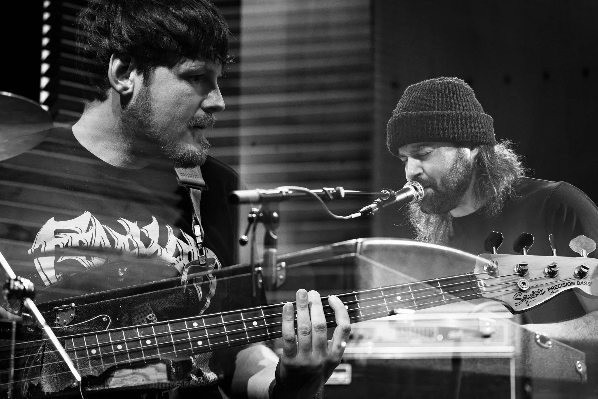 Two musicians, one playing bass guitar and the other singing into a microphone, in a recording studio.