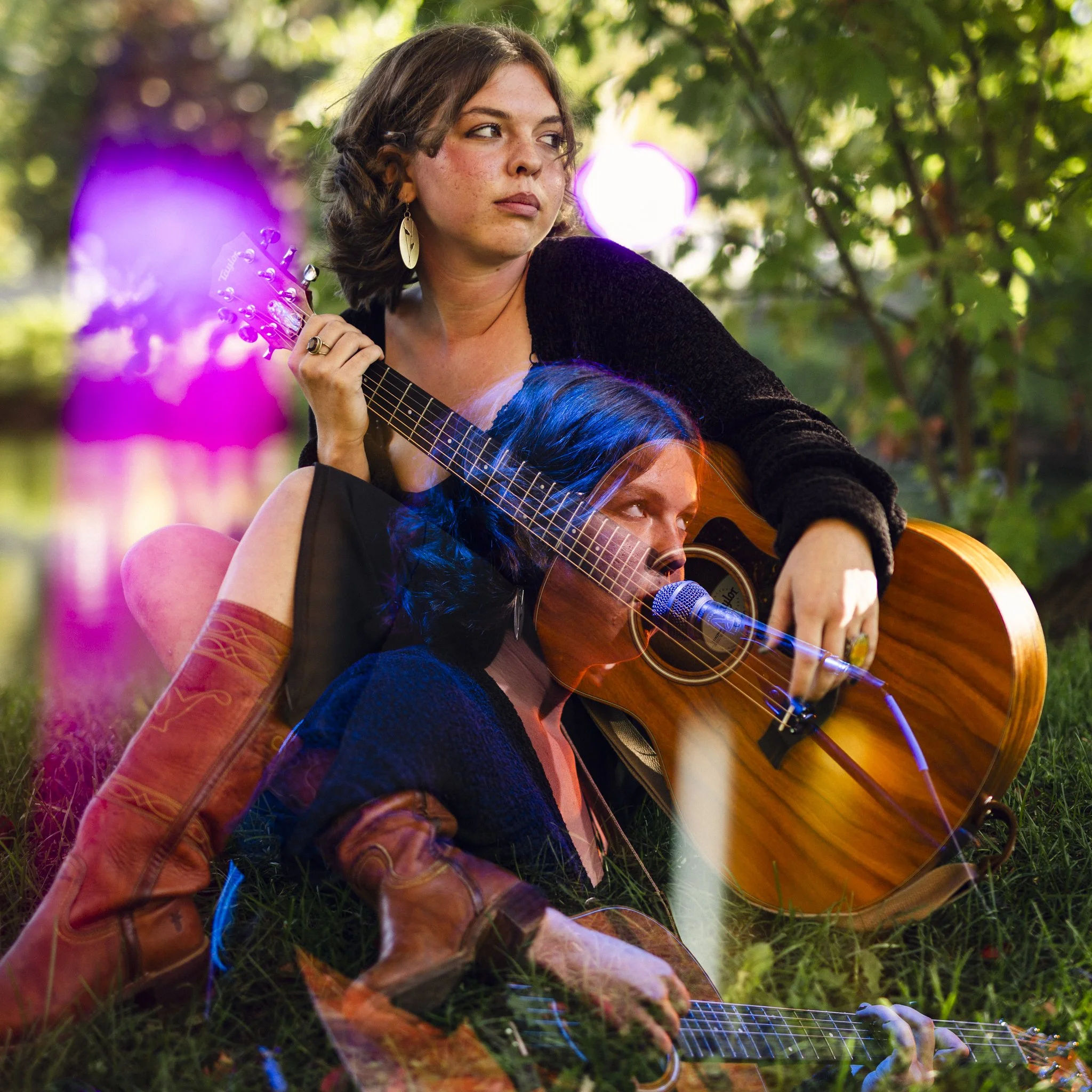 Two women sitting on grass outdoors with guitars, one is singing into a microphone and the other is holding her guitar, surrounded by green trees and colorful light effects.