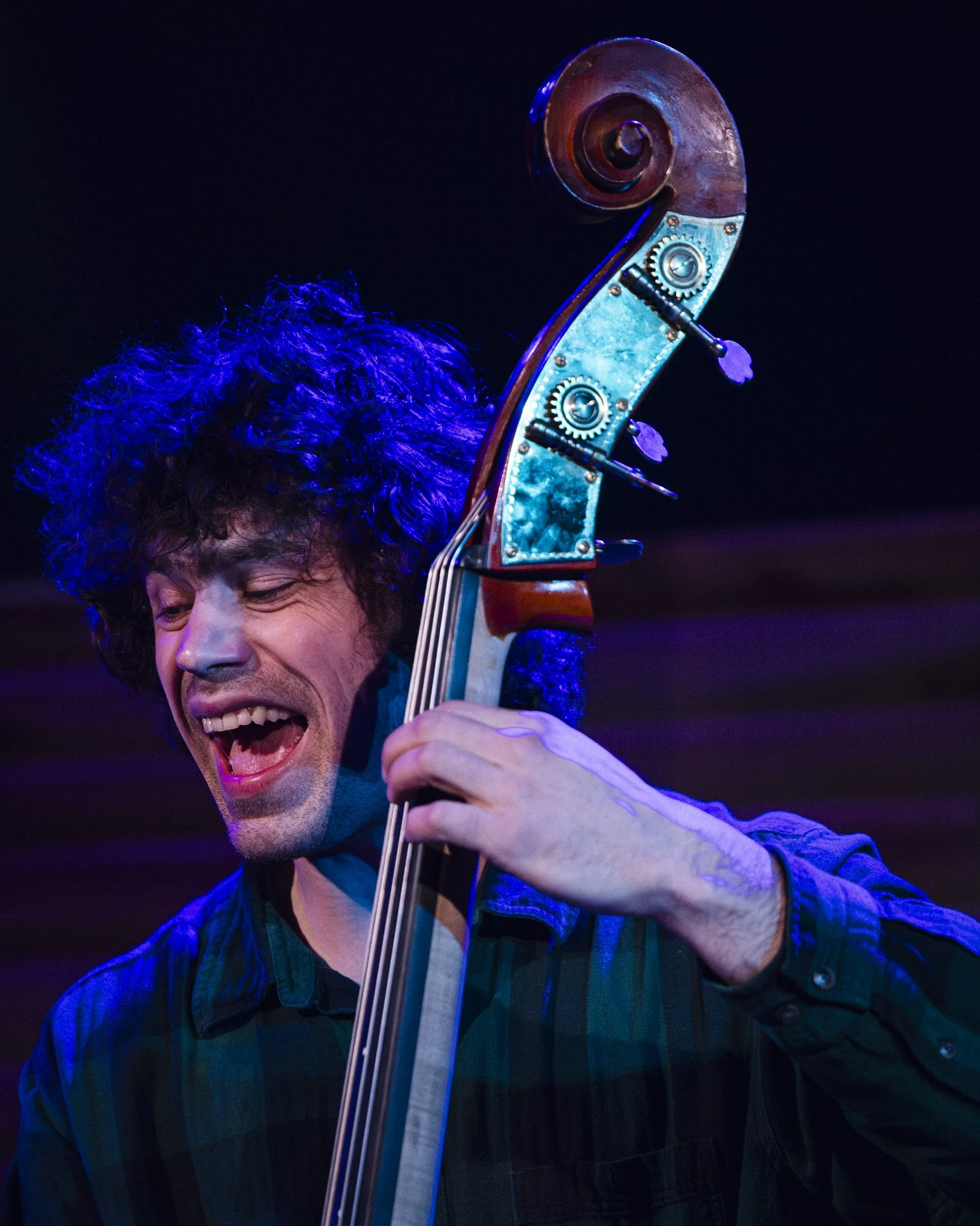 Musician playing double bass with a joyful expression on stage, illuminated by colorful stage lighting.