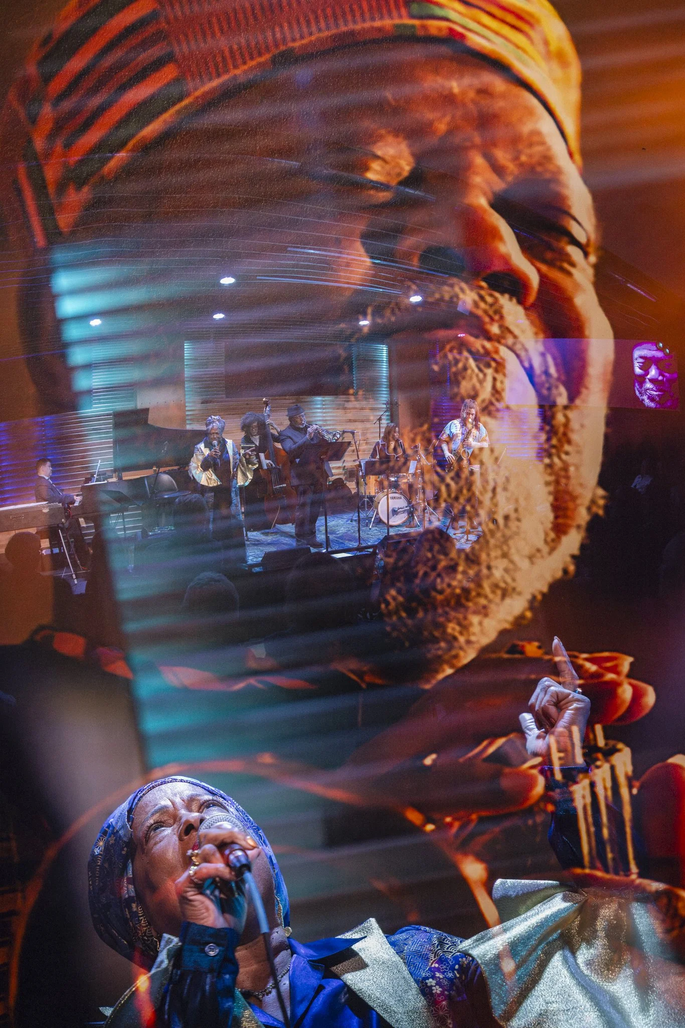 A double exposure image of a woman singing into a microphone and a large close-up face of a man, overlaid with a live band performing on stage.