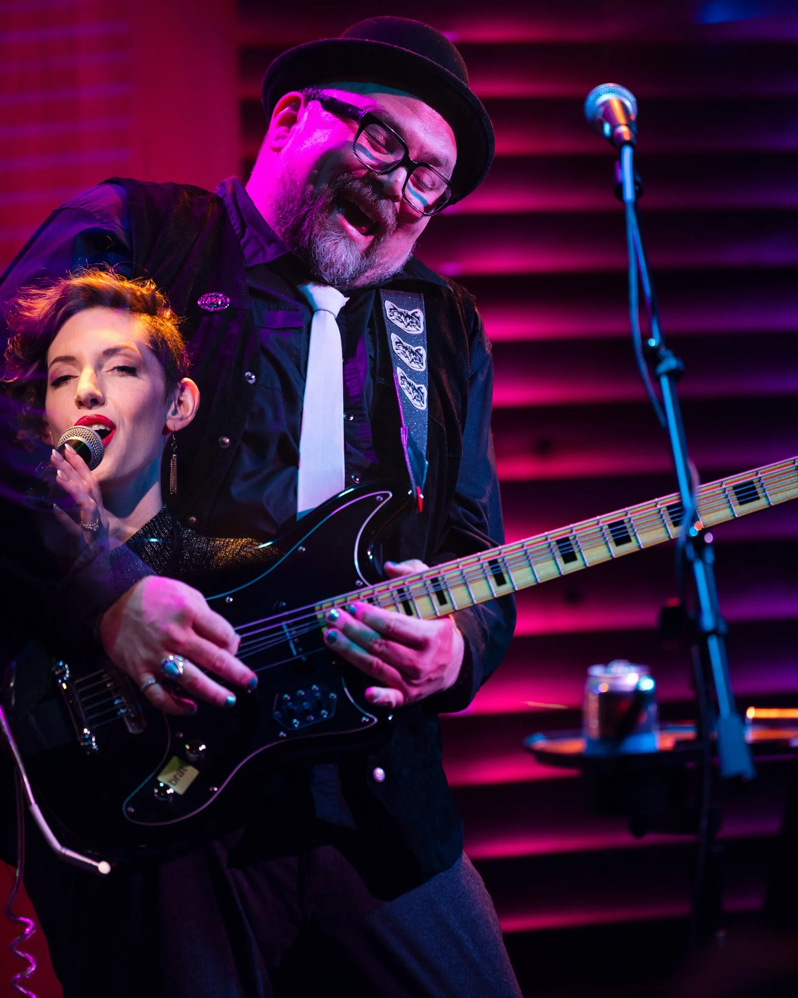 A male guitarist playing electric guitar and a female singer holding a microphone on stage with colorful lighting.