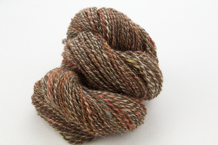 Handspun yarn. One ply is from a batt containing Bluefaced Leicester Wool, Tussah Silk, brown Merino Wool, red Kid Mohair, Angelina, and more. The other ply is natural colored Shetland blended with cinnamon and white Alpaca.