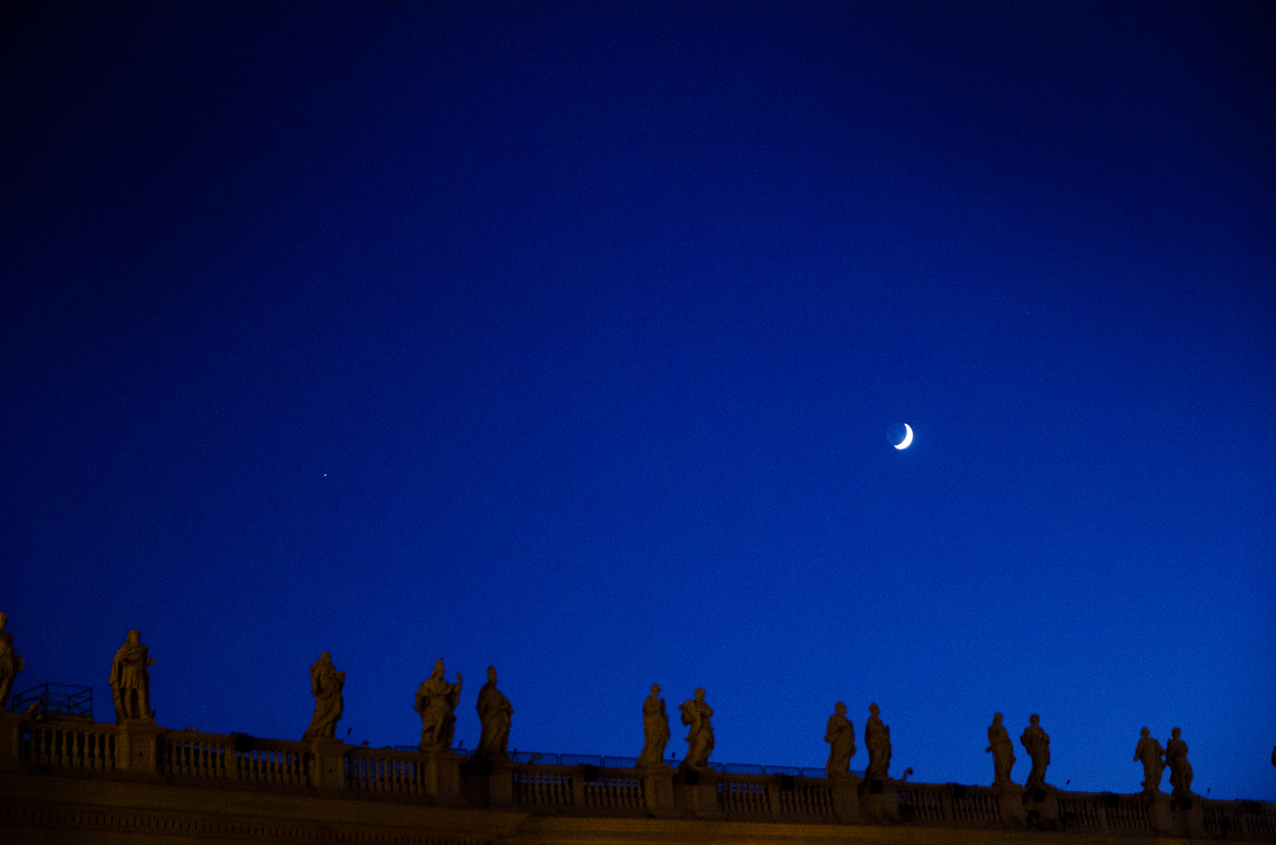 Overlooking the Main Square outside of St. Peter's Basilica, these statues stand tall silhouetted by a crescent moon in Vatican City, Italy. 