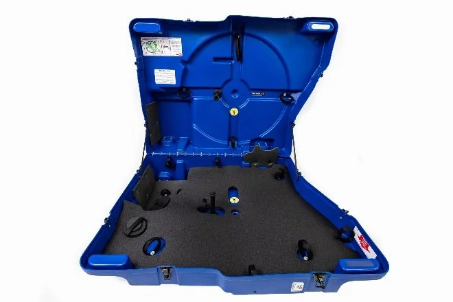 a blue bike travel case opened up, showing the interior foam, many loop strap mounting points, and a sticker of instructions