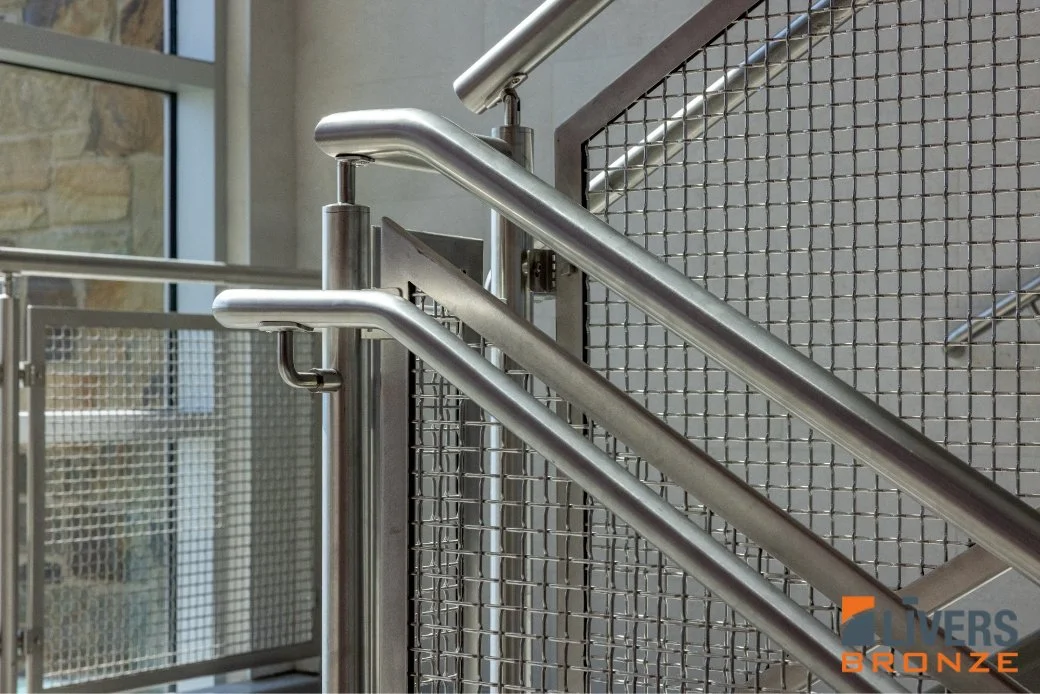 Stainless steel school railing with wire-mesh infill panels along an interior stair