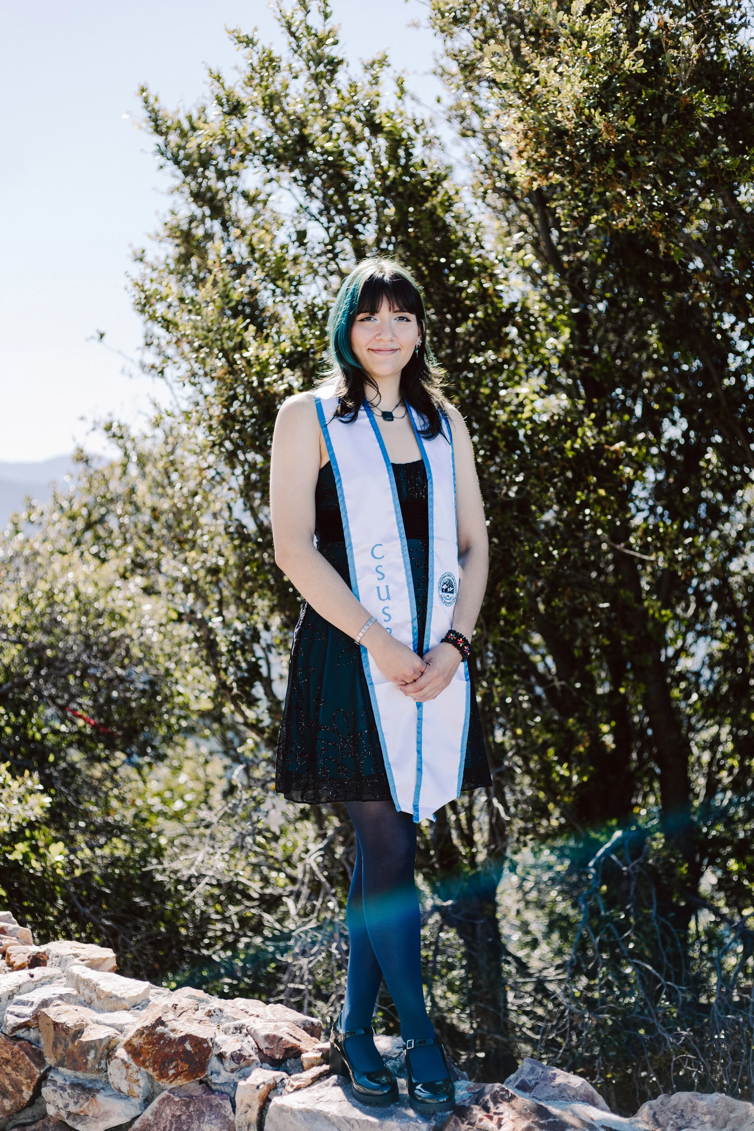 CSUSB graduate posing above the San Bernardino Mountains wearing her sash