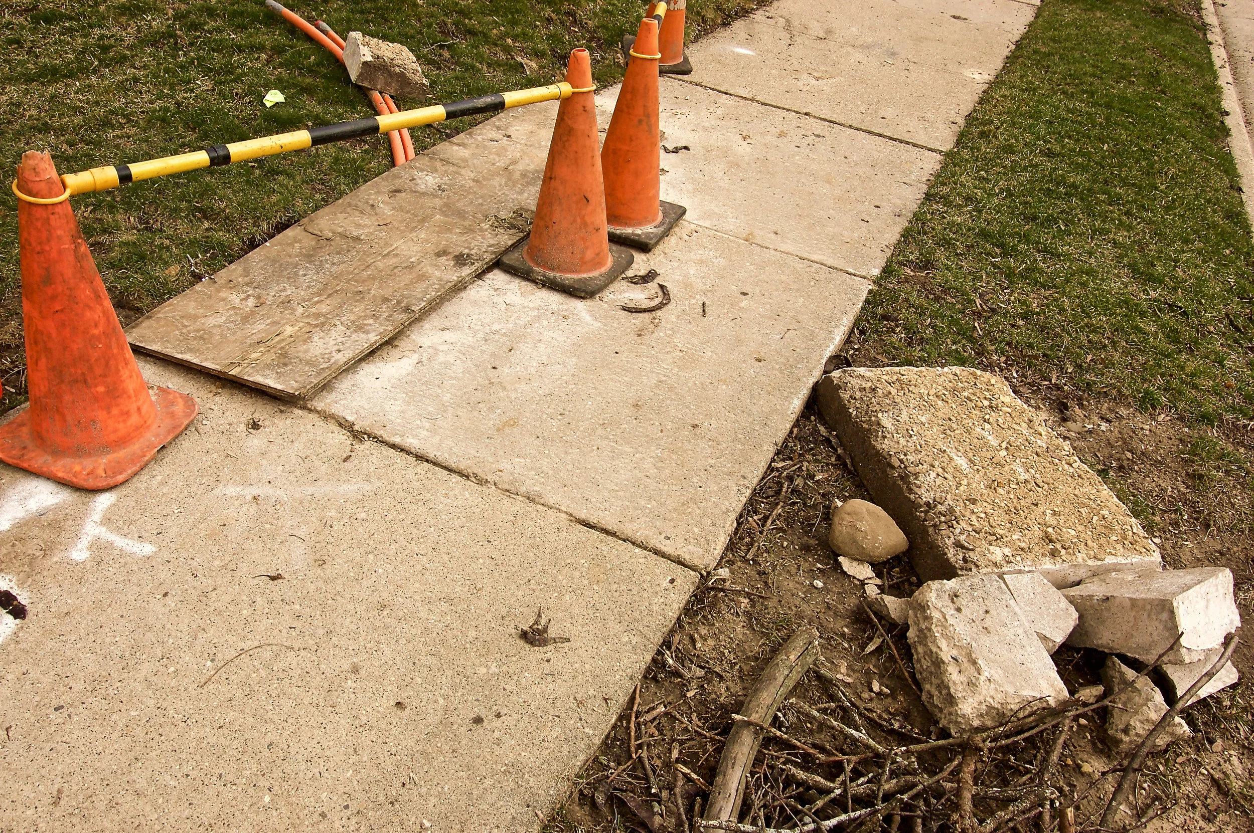 Poorly marked and covered hole. Scattered sidewalk pieces. (One of several images of a sloppily-managed cable laying project.)