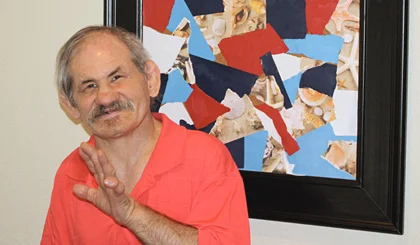  David poses next to one of his framed collage pieces he makes using scraps of ripped paper.