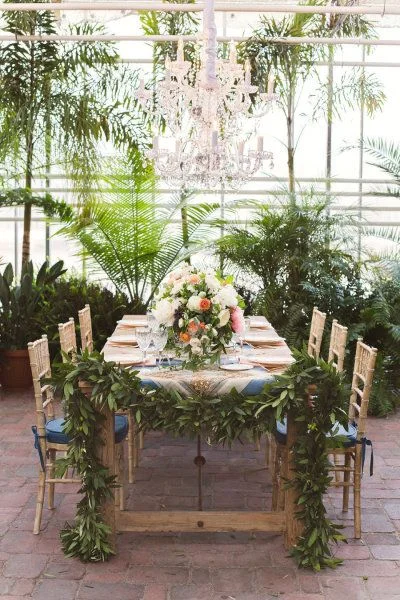 Gold Tiffany chairs, floral runner on the table ends and surrounded by leafy green palms.