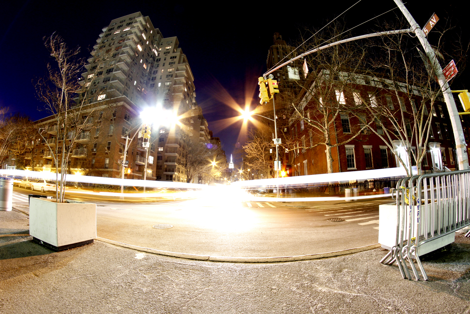 Cars making left and right turns at the foot of Fifth Ave., with The Empire State Building in the distance.
