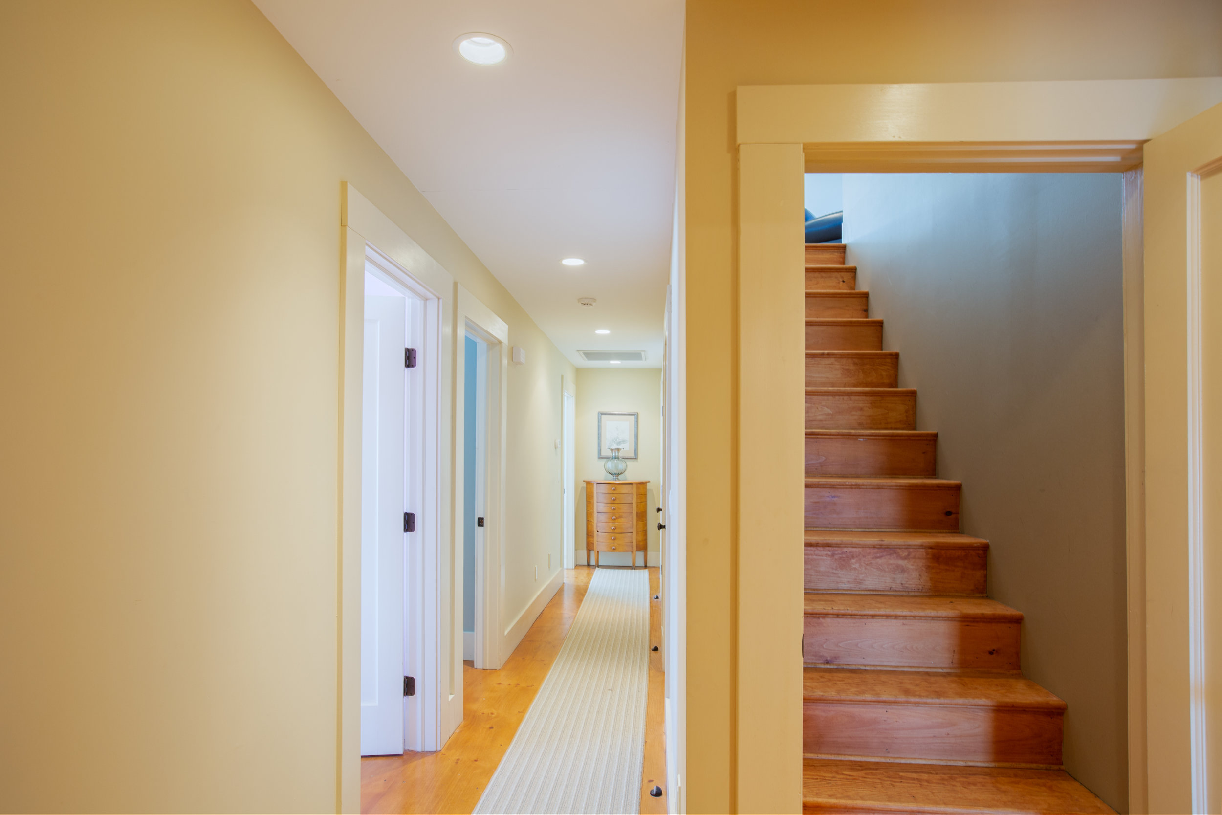  Hallway and stairway view.  White running leads to end of the hall.  Two white doors are next to one another leading into to separate rooms.  The stairs are wooden  and go straight up. 