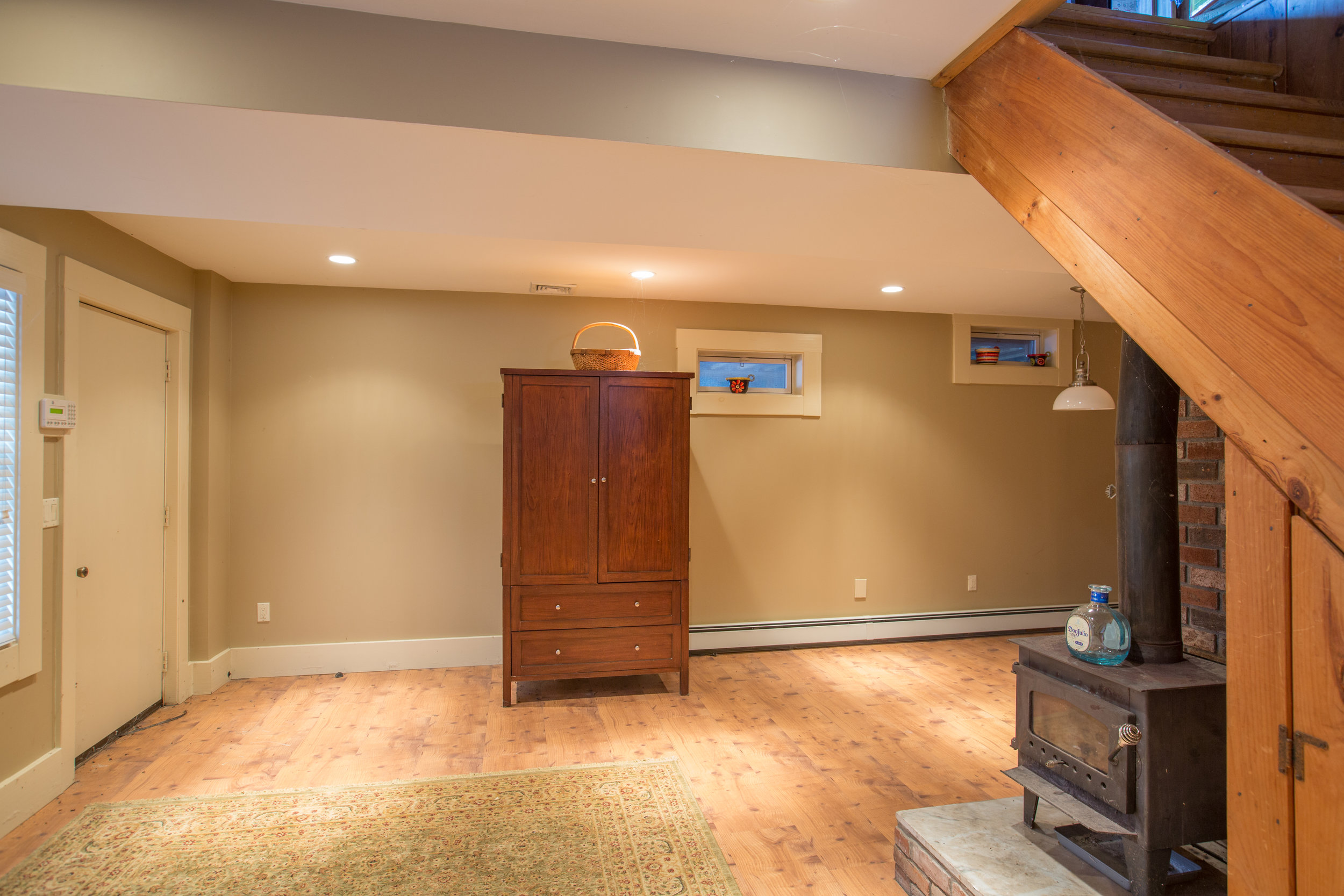  Finished basement that has a wood burning stove to the right side underneath the stairway.  An armor  sits nicely on the back wall with a basket on top.  Floors are a natural hardwood. 