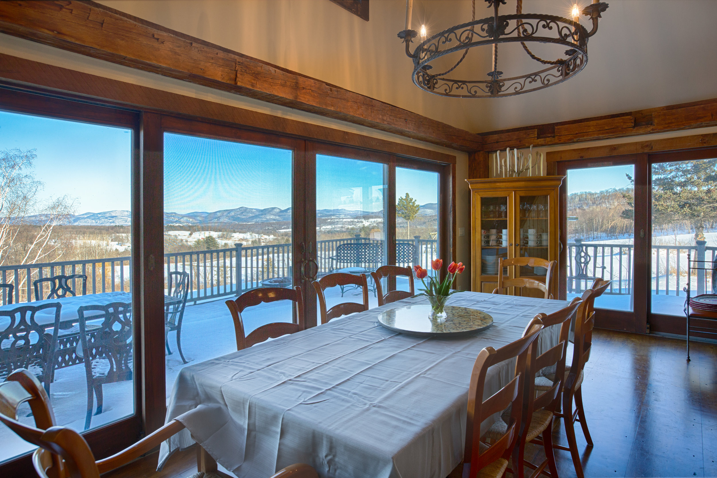  Wide open view looking into dining room. Dining room walls are lined with floor to ceiling windows that overlook a deck with a Mountain View. There is a table in the center of the dining room with multiple chairs and an armour tucked in the corner o