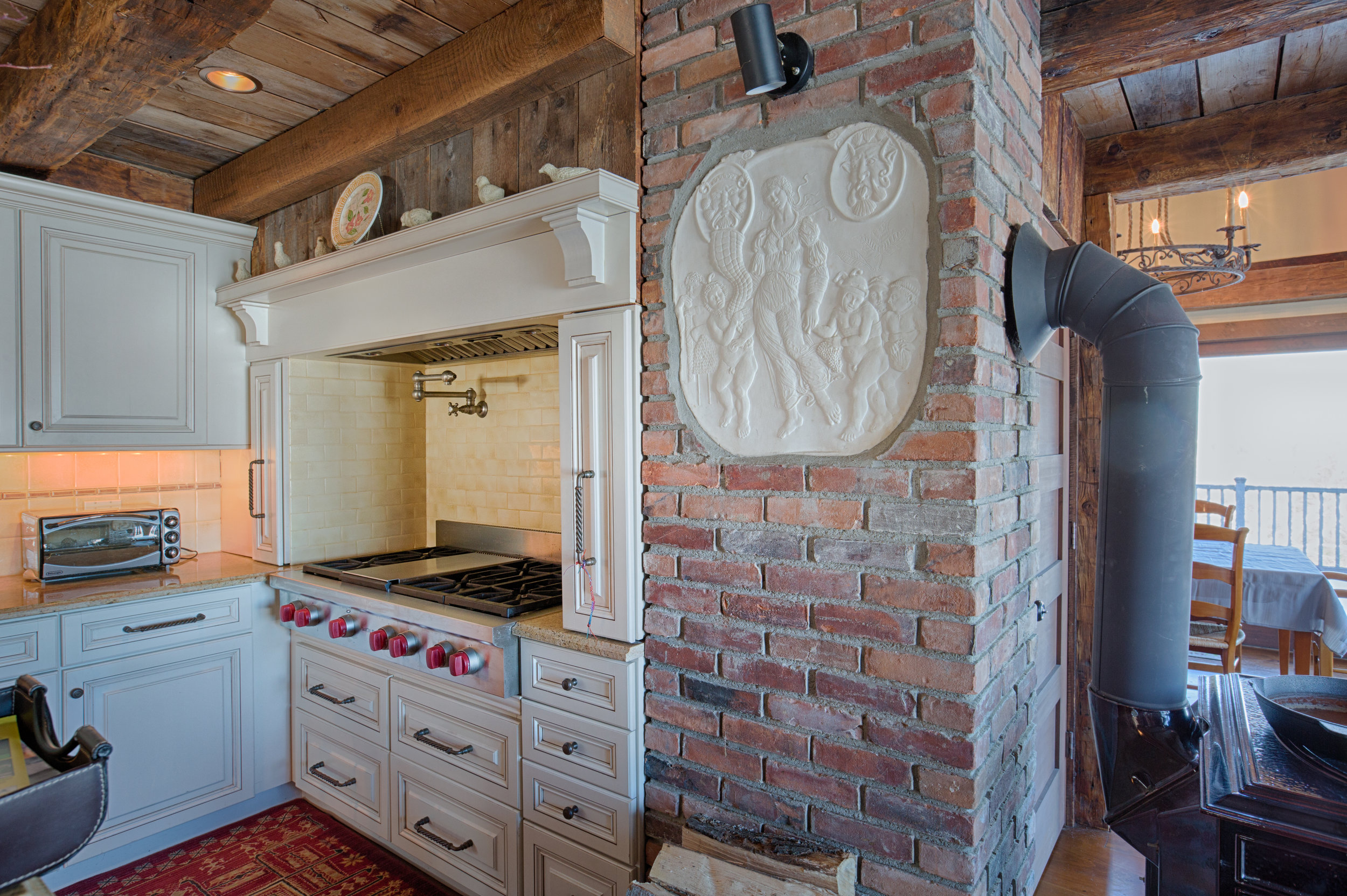  Kitchen stove top nook.  Brick wall surrounds the high-end cook top with drawers underneath.  A built in vent is above the cook top and a pot filler faucet is on the back wall. 