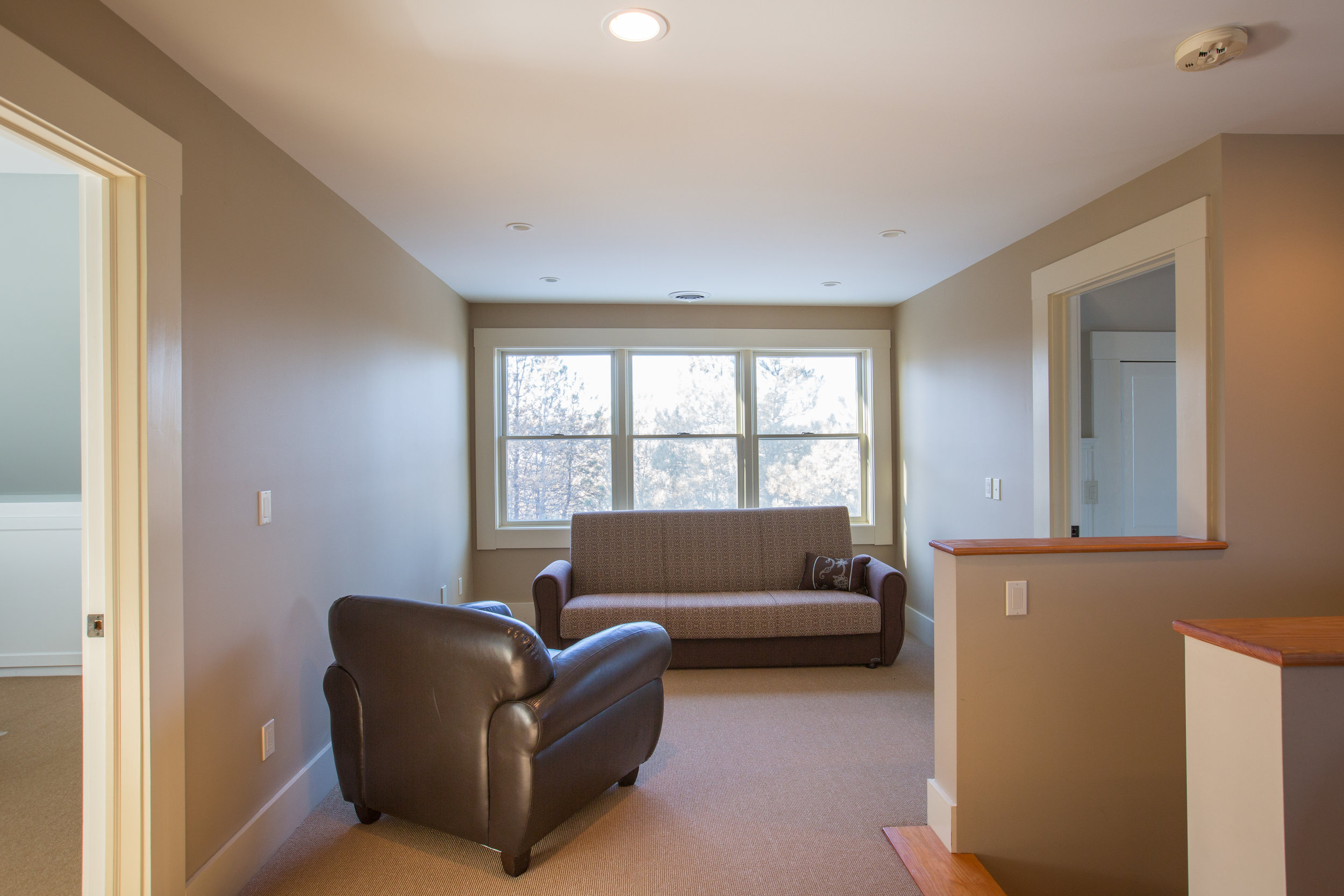  Upstairs sitting area.  To the right of the stair case the space is used as a sitting area.  Three windows are next to one another with a futon against the windows and a chair is positioned nicely center left of photo. 