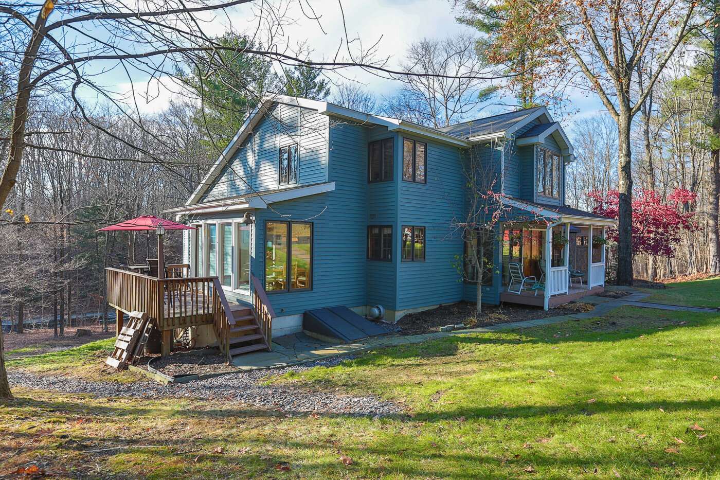  Outside of home with deck to the left of the image with a red umbrella opened on the deck.  