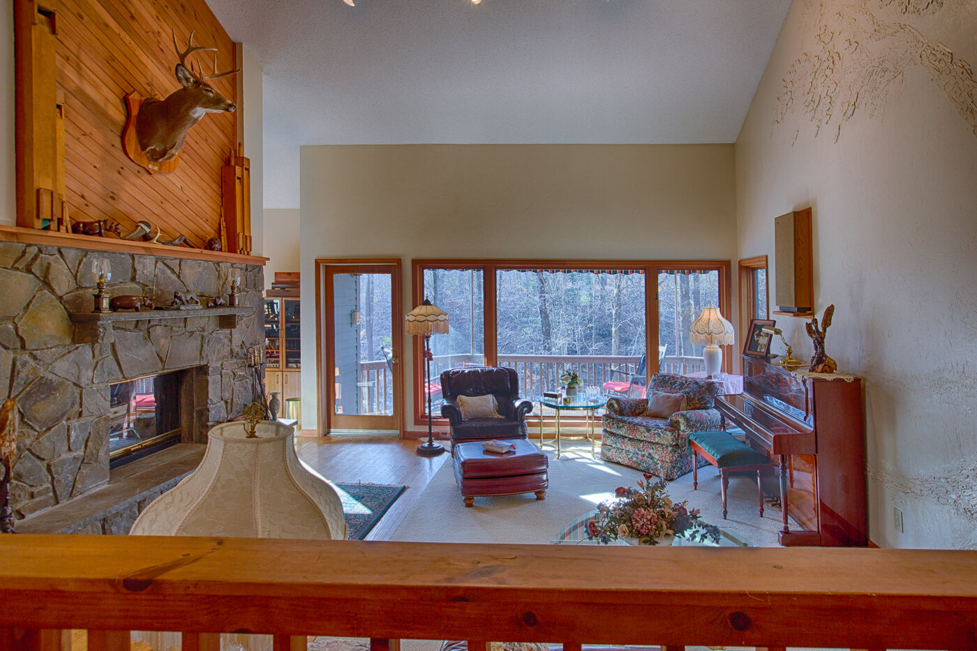  Inside living area with large stone fireplace and cathedral ceilings.  Deer head is hanging above the fire place and a sliding glass door that opens to the outside porch. 