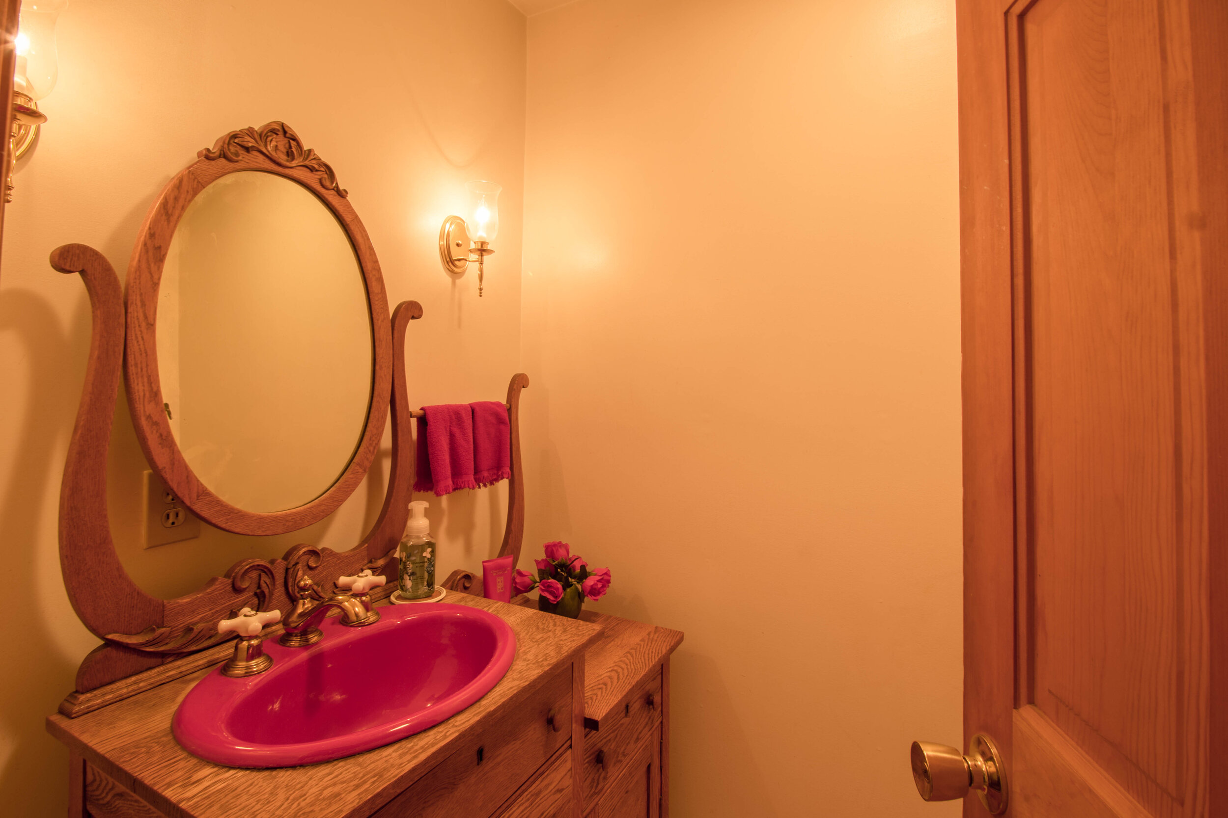  Smaller bathroom with single vanity, circle mirror above the vanity and a pink sink. 