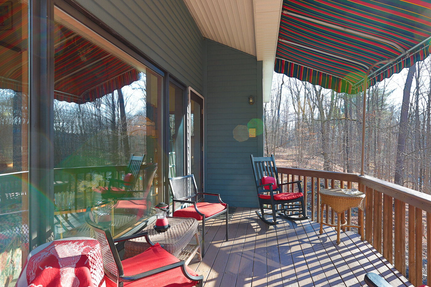  Covered porch with awning covering it. Red patio furniture is furnishing the deck. 