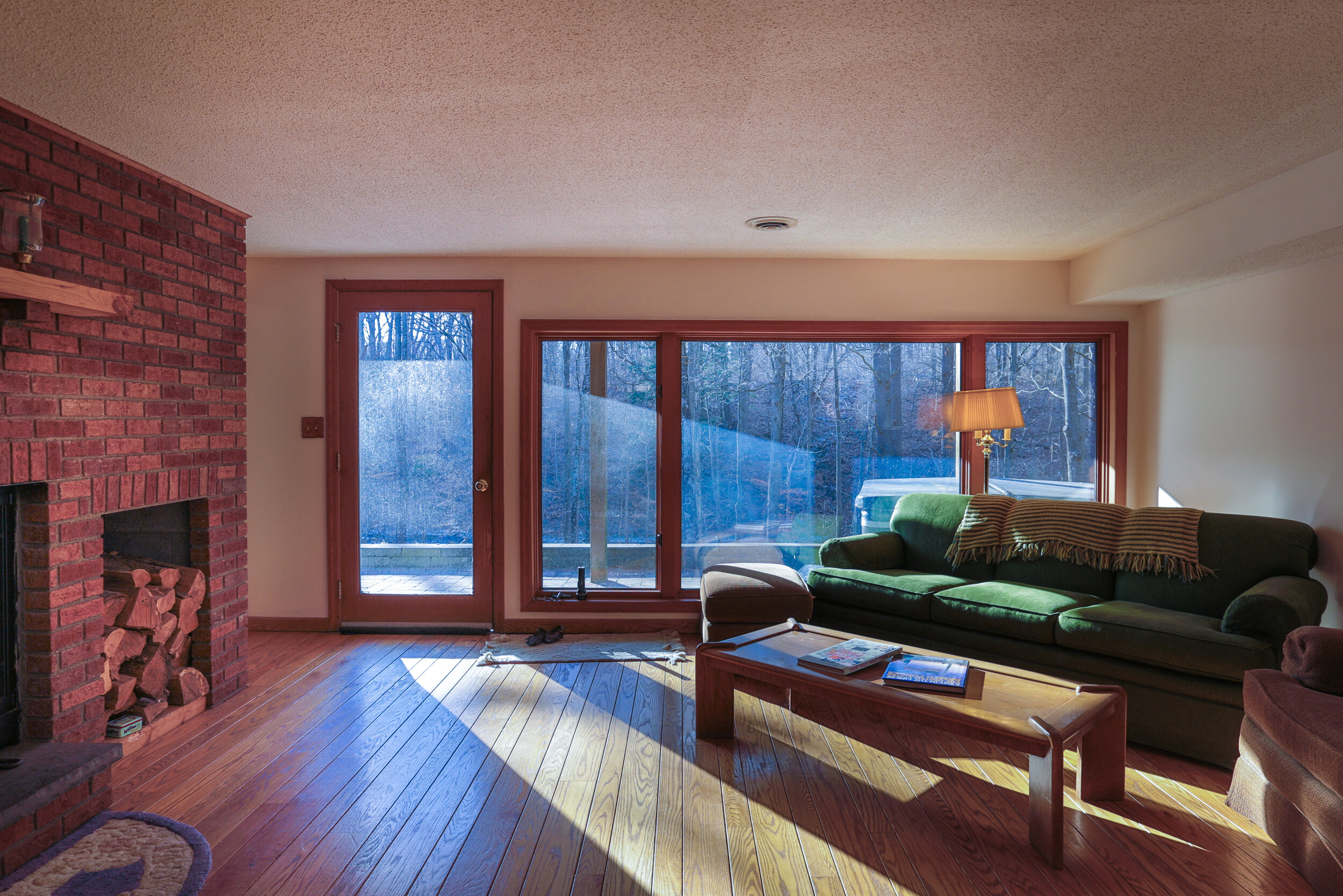  Additional living space with brick fireplace and a built in wood shelf next to the fireplace. Hardwood floors, sliding glass door in the background and a green kiddie corner couch. 