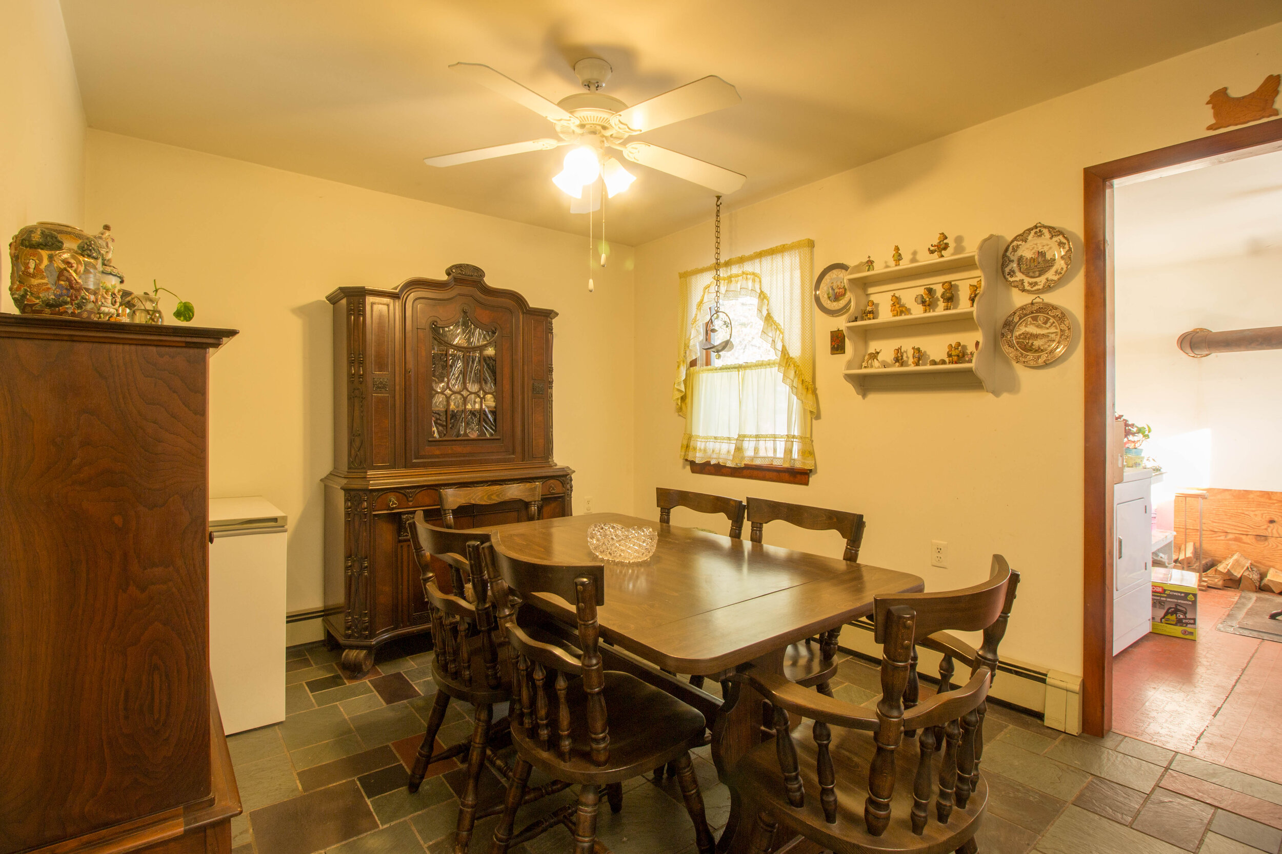  Kitchen with table in the center of it.  Decorations on the wall and a hutch on the back wall in center of the room. 