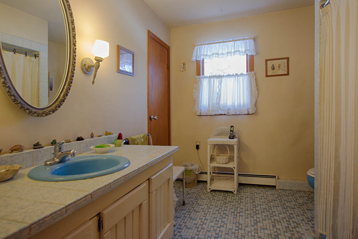  Bathroom with blue and white small tile floor, blue sink encased in a vanity.Circle mirror above the sink/vanity combination.  