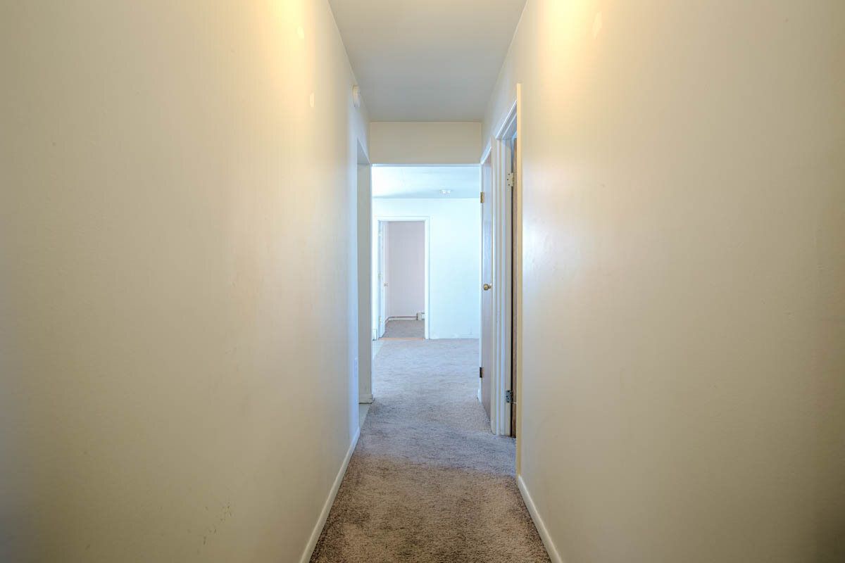  Hallway looking down into living room.  Hallway has a nice gray carpet and there are white walls. 