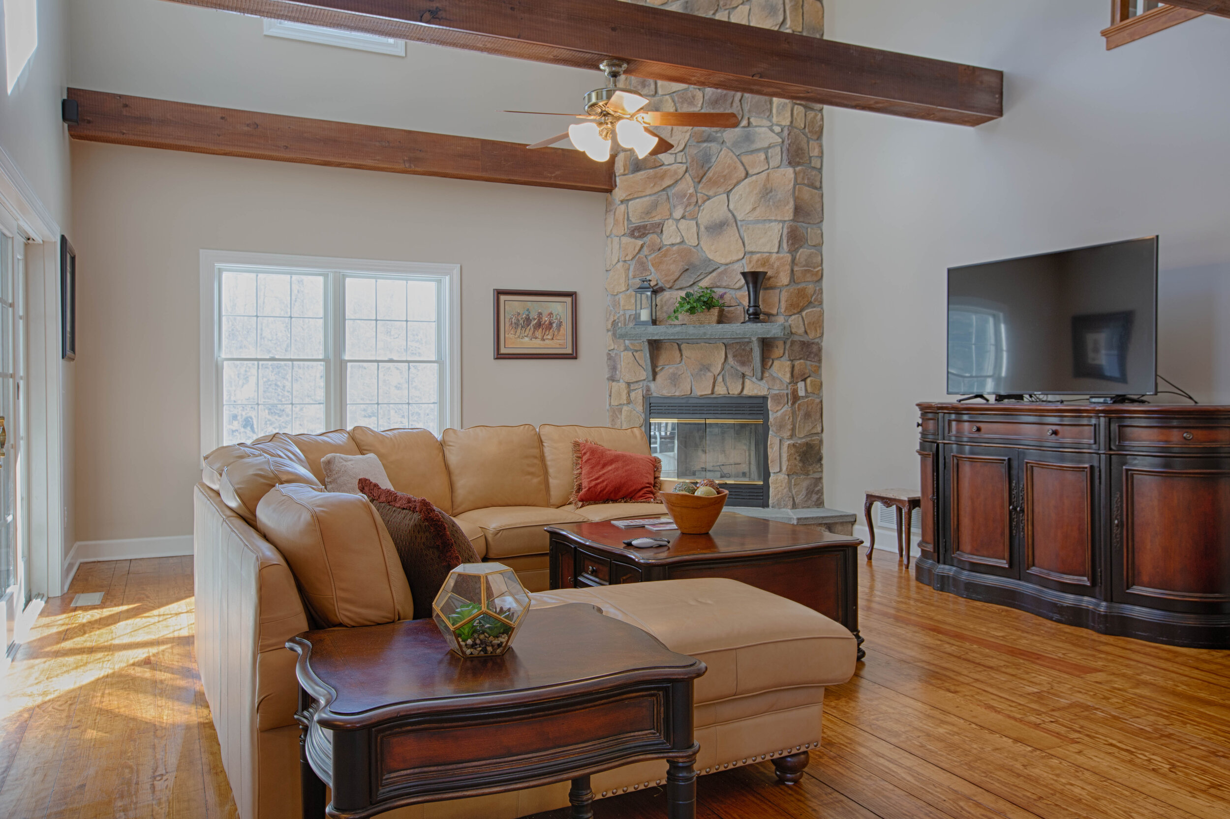  Light brown sectional couch encompassing a table. Hardwood floors and a custom bar to the right of the photo. 