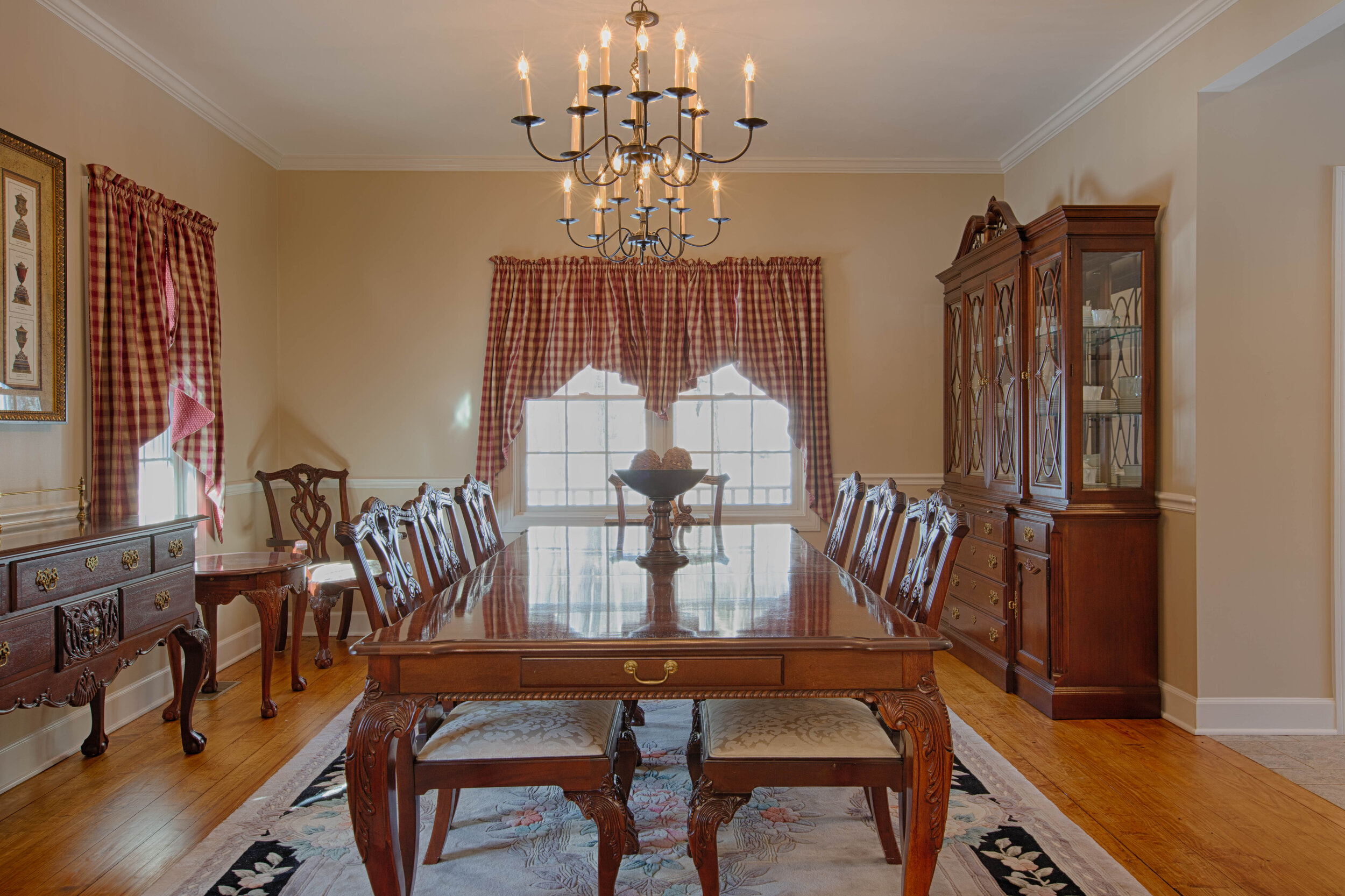  Dining room with large table in center along with a double window in the center of the wall and a hutch to the right of the photo. 