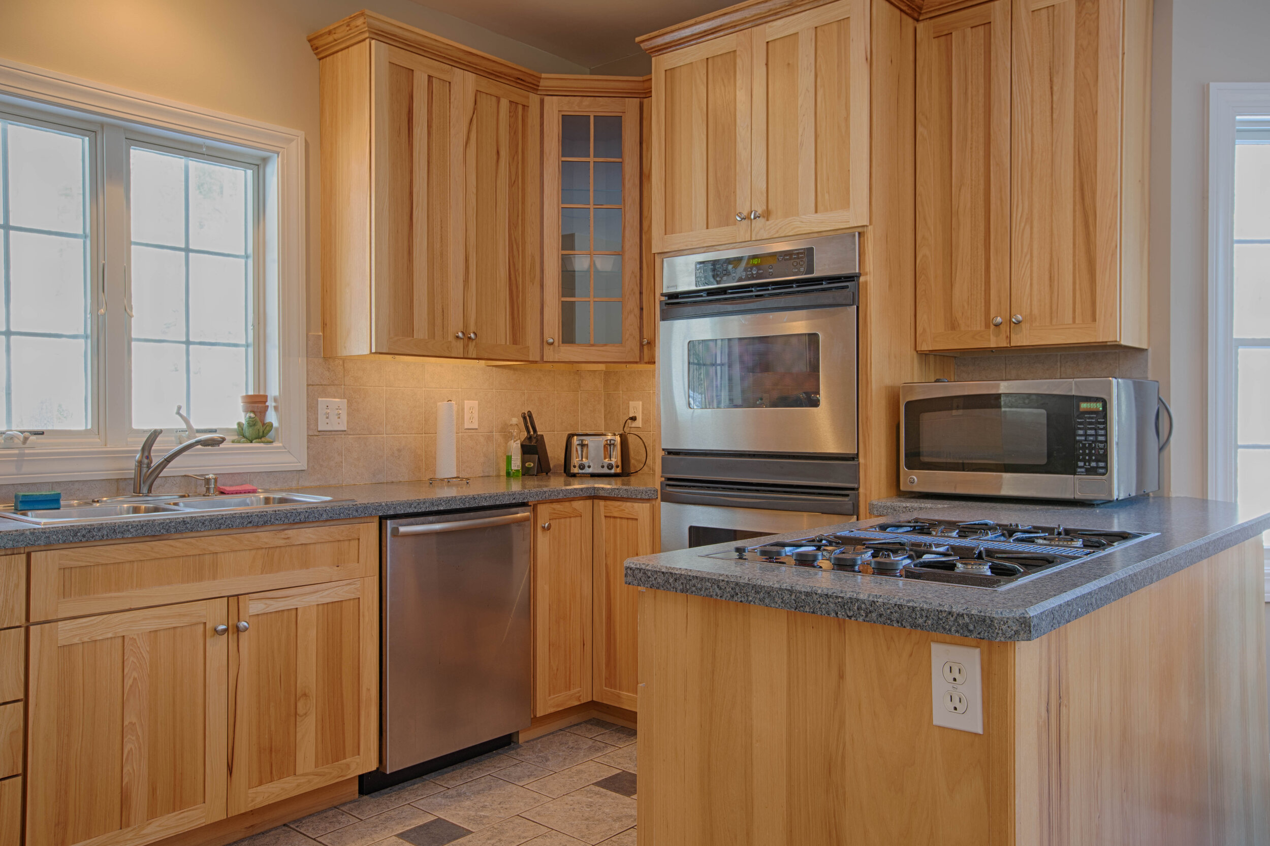  Kitchen with tasteful wood cabinets, double oven, stainless steel dishwasher with a greenish color countertop. 