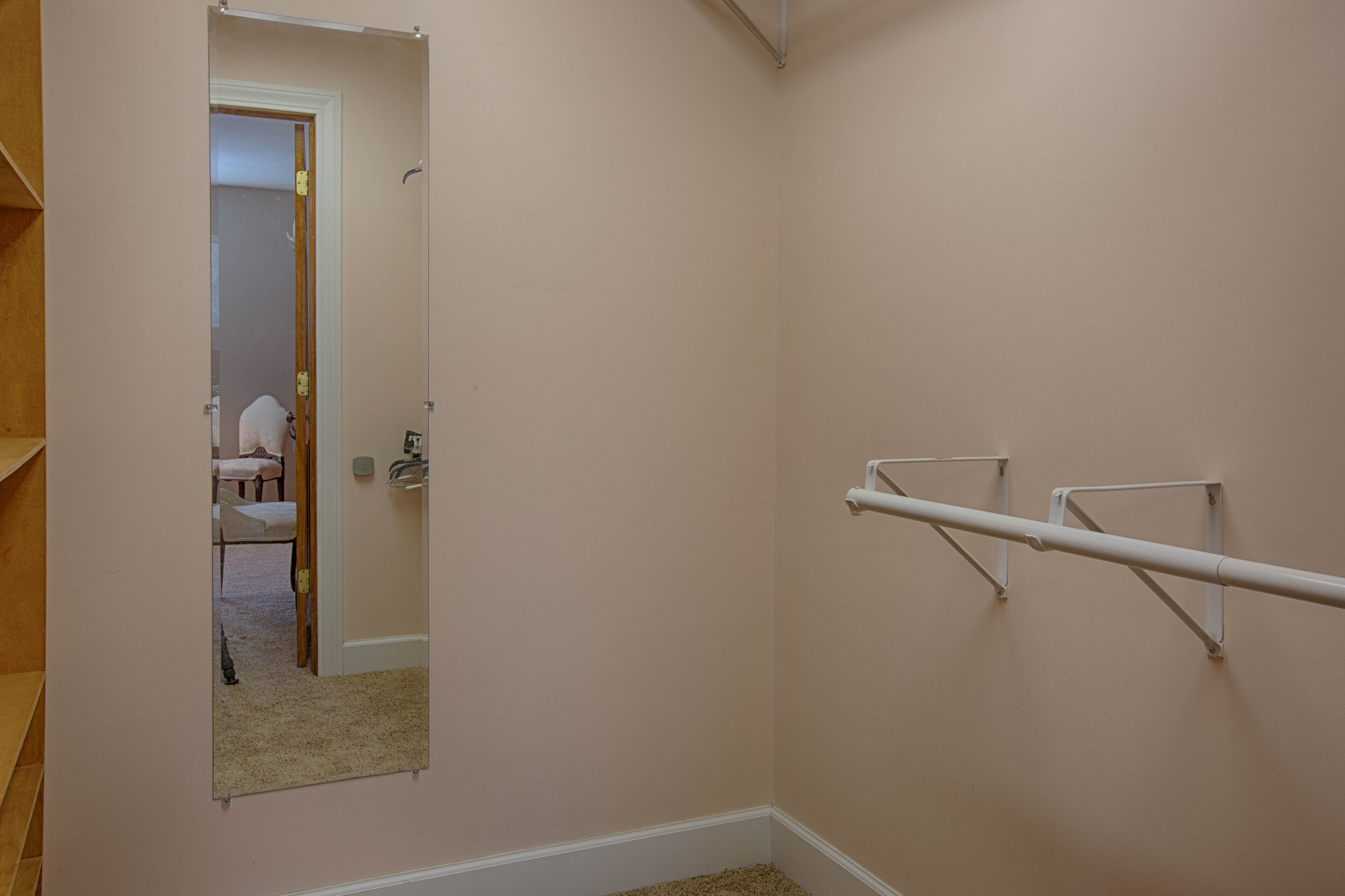  Walk in closet with mirror on the wall, and clothing rack attached to the right of the wall. 