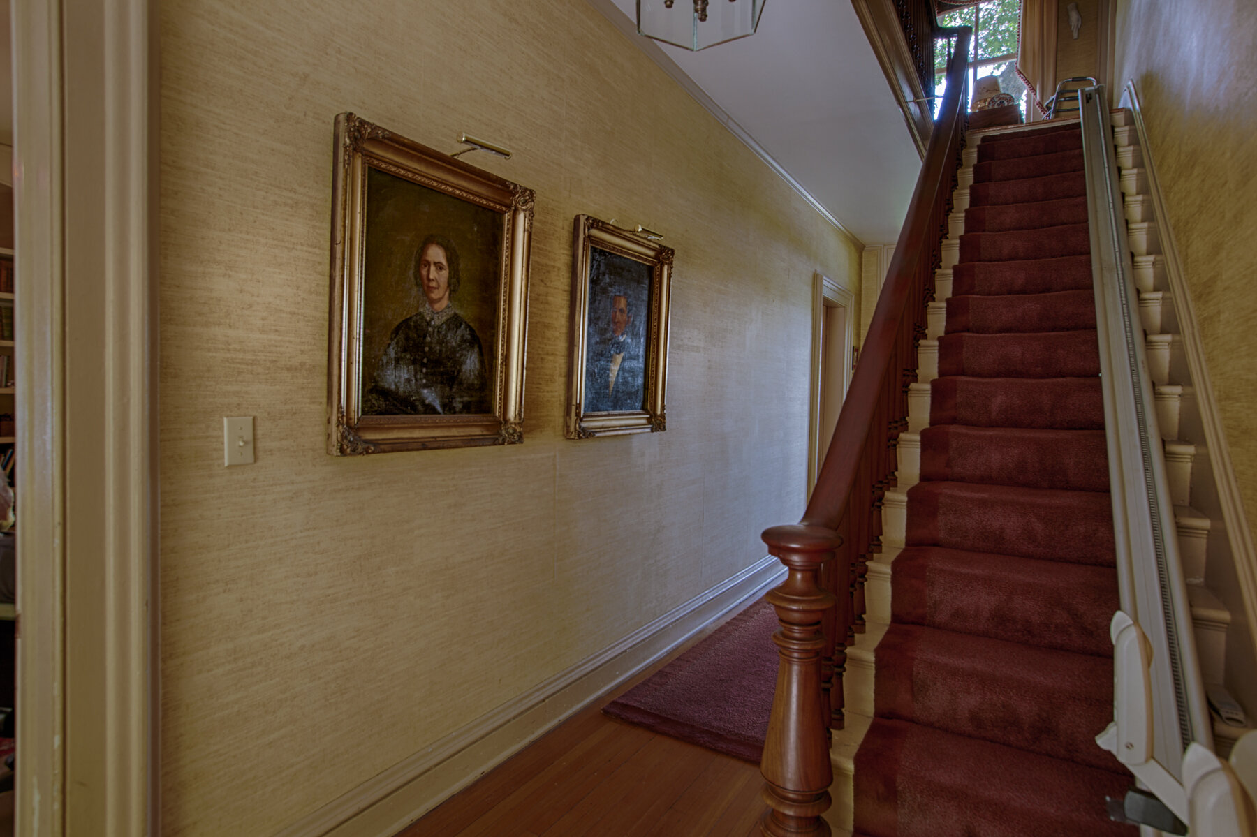  Staircase to the right with red carpeting. Two pictures hang on the wall to the left. 