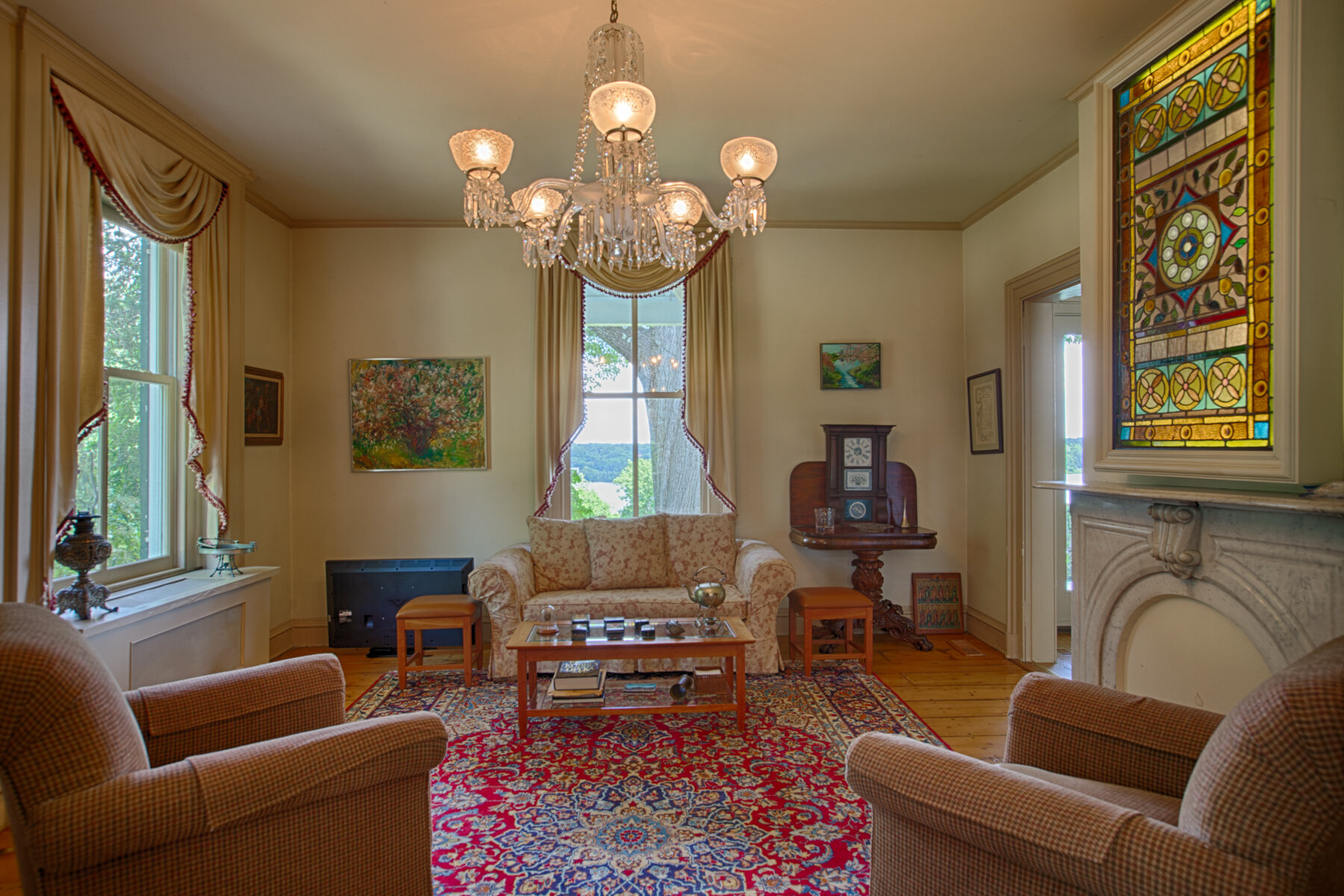  Sitting room with red throw rug in the center and two chairs on each side.  Picture hangs above non working fireplace. 