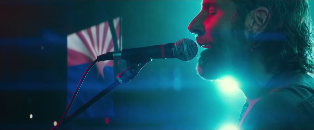 Jack singing during Shallow. He is illuminated in a majority of cyan with subtle nodes of red on his face.