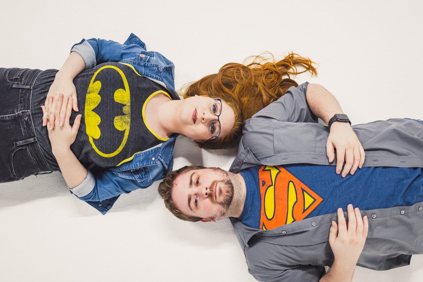 couple lies on floor with batman and superman t-shirts