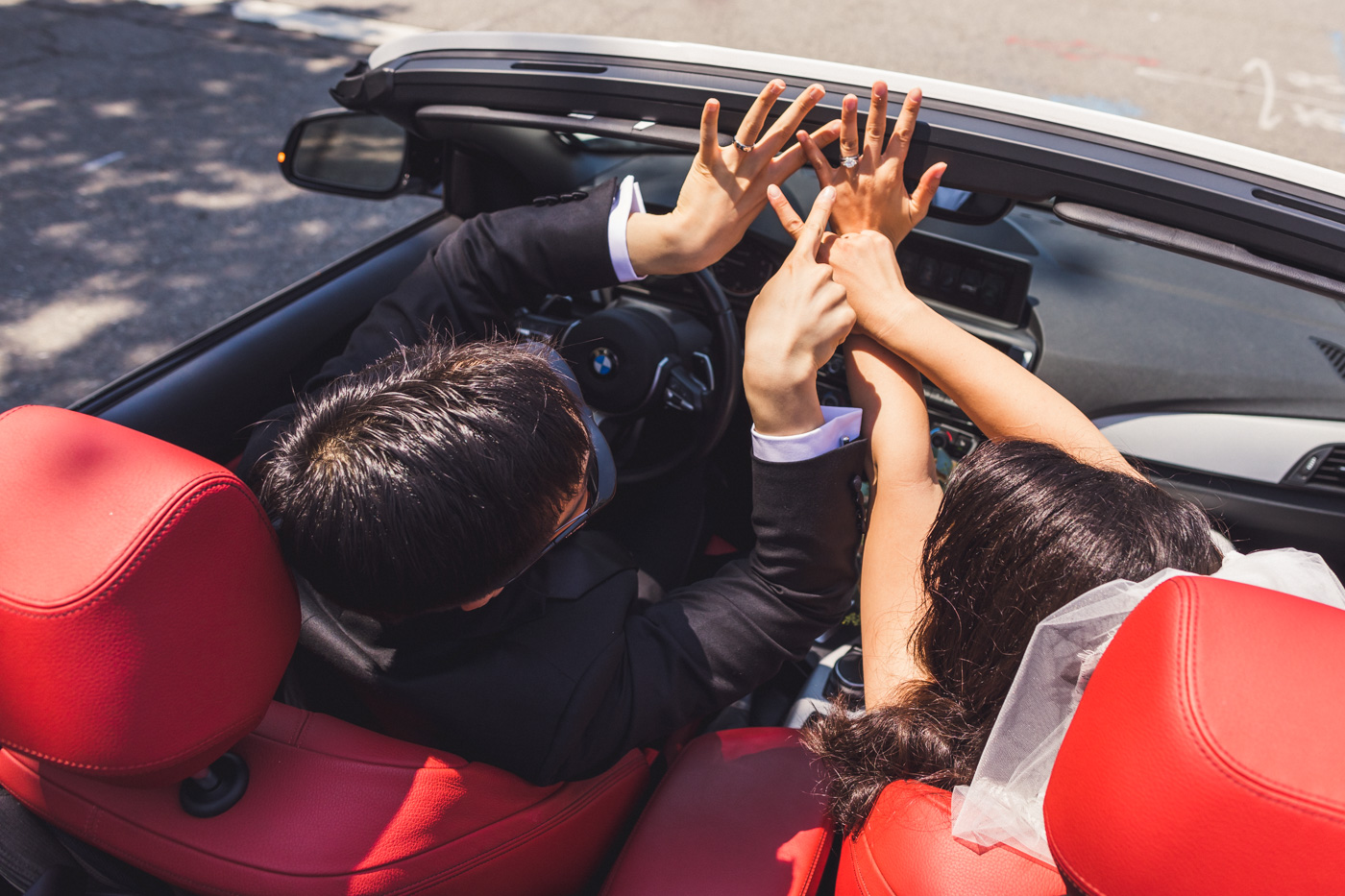 bride-and-groom-showing-off-rings-in-convertible