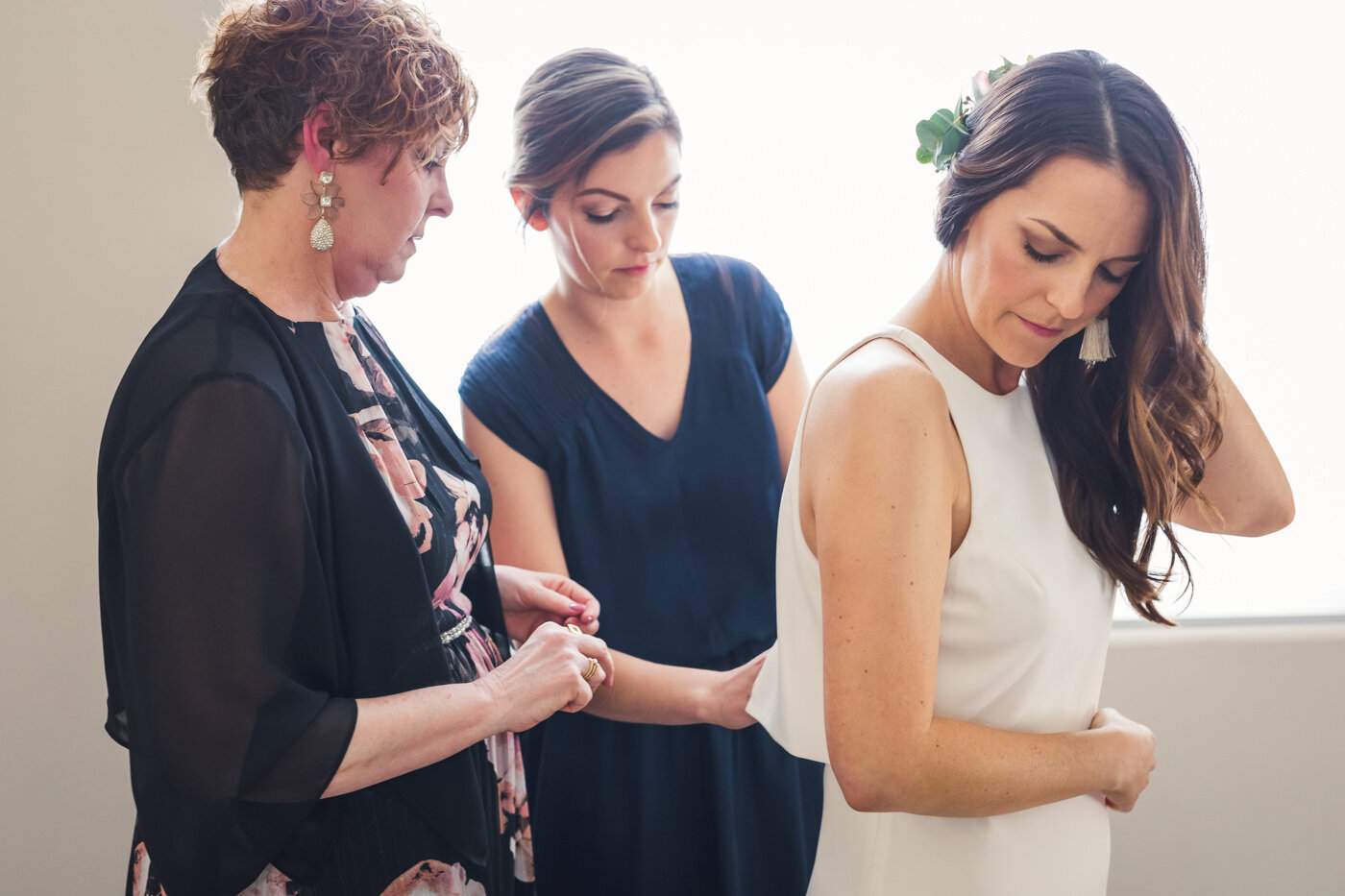 bride-putting-dress-on-with-mom-and-sister