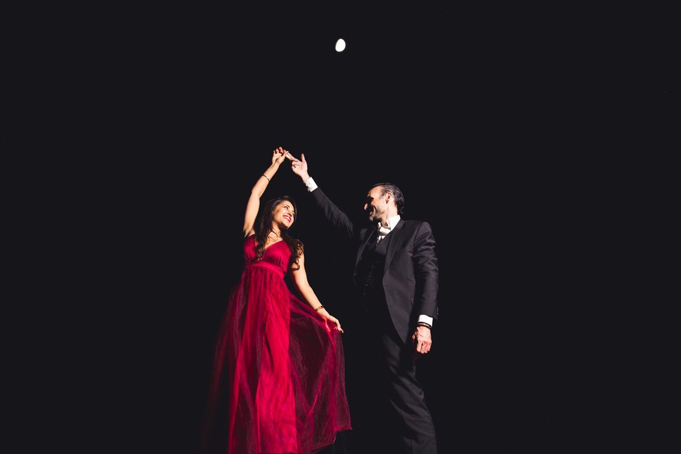 man twirls fiance under the moon at night during engagement session