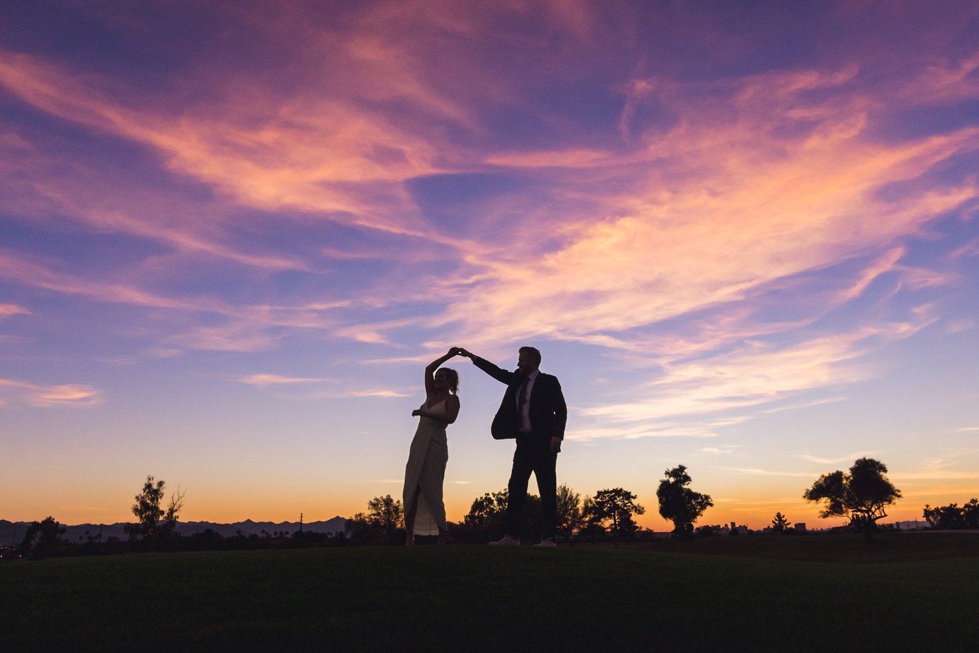 groom twirls wife in silhouette at sunset