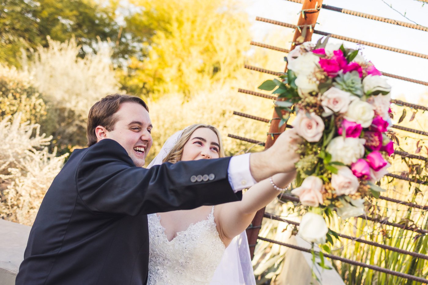 bride and groom having fun holding up bouquet together laughing