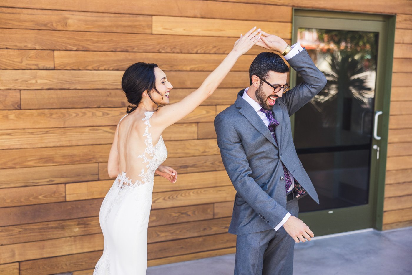 bride twirls groom in front of wooden wall