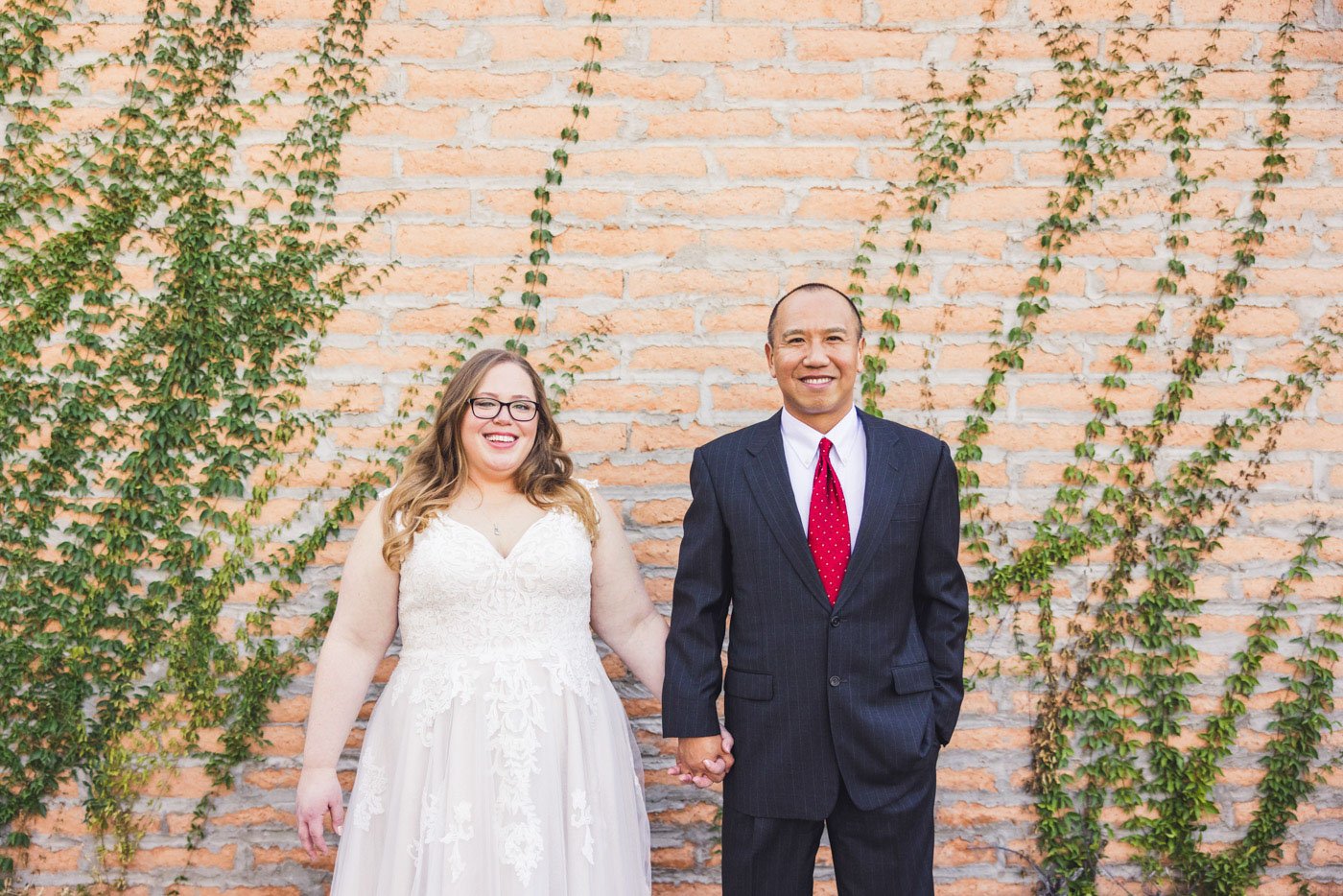 bride and groom hold hands in front of ivy covered brick wall